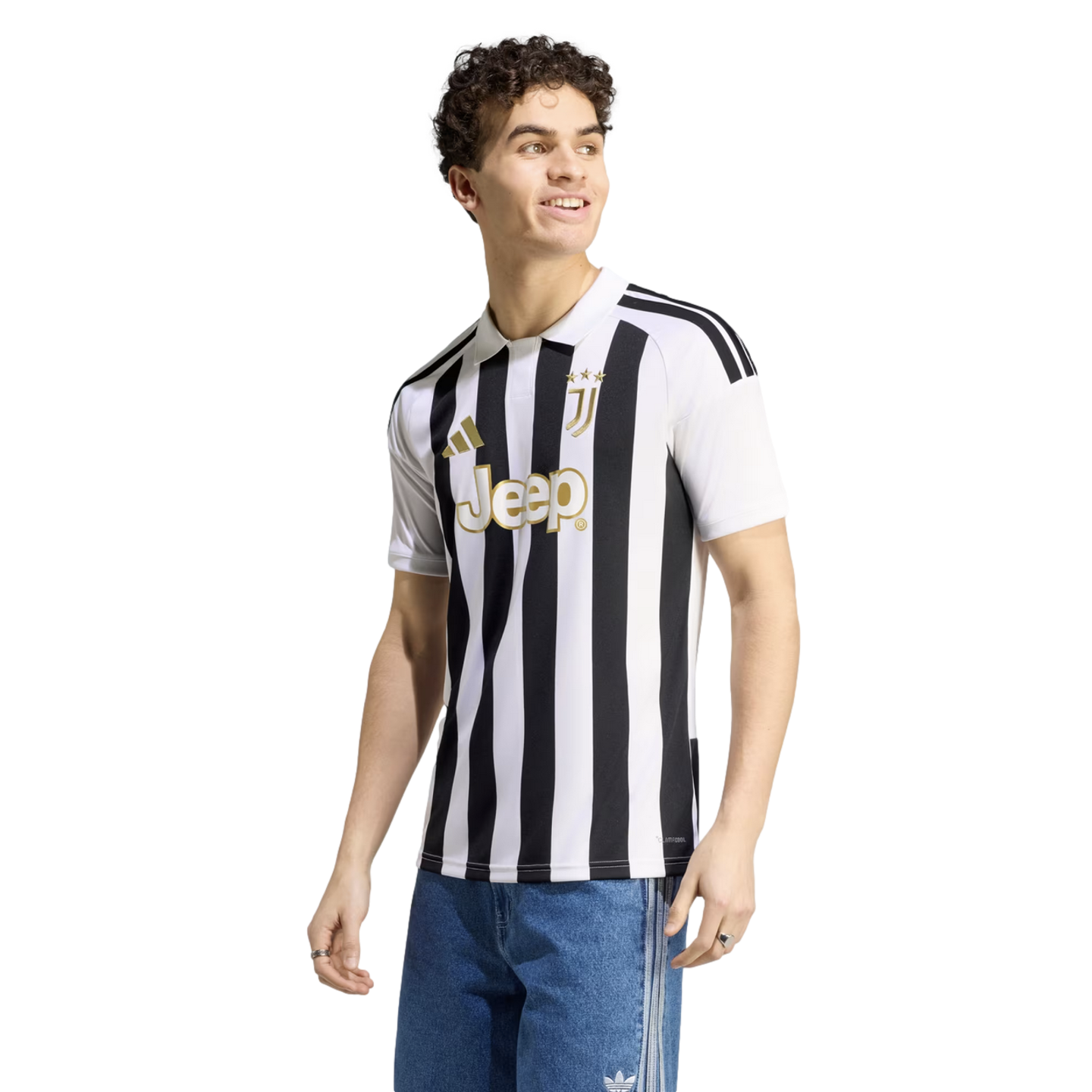 A smiling man wearing a Juventus black and white striped football jersey with gold accents and blue jeans, against a white background.