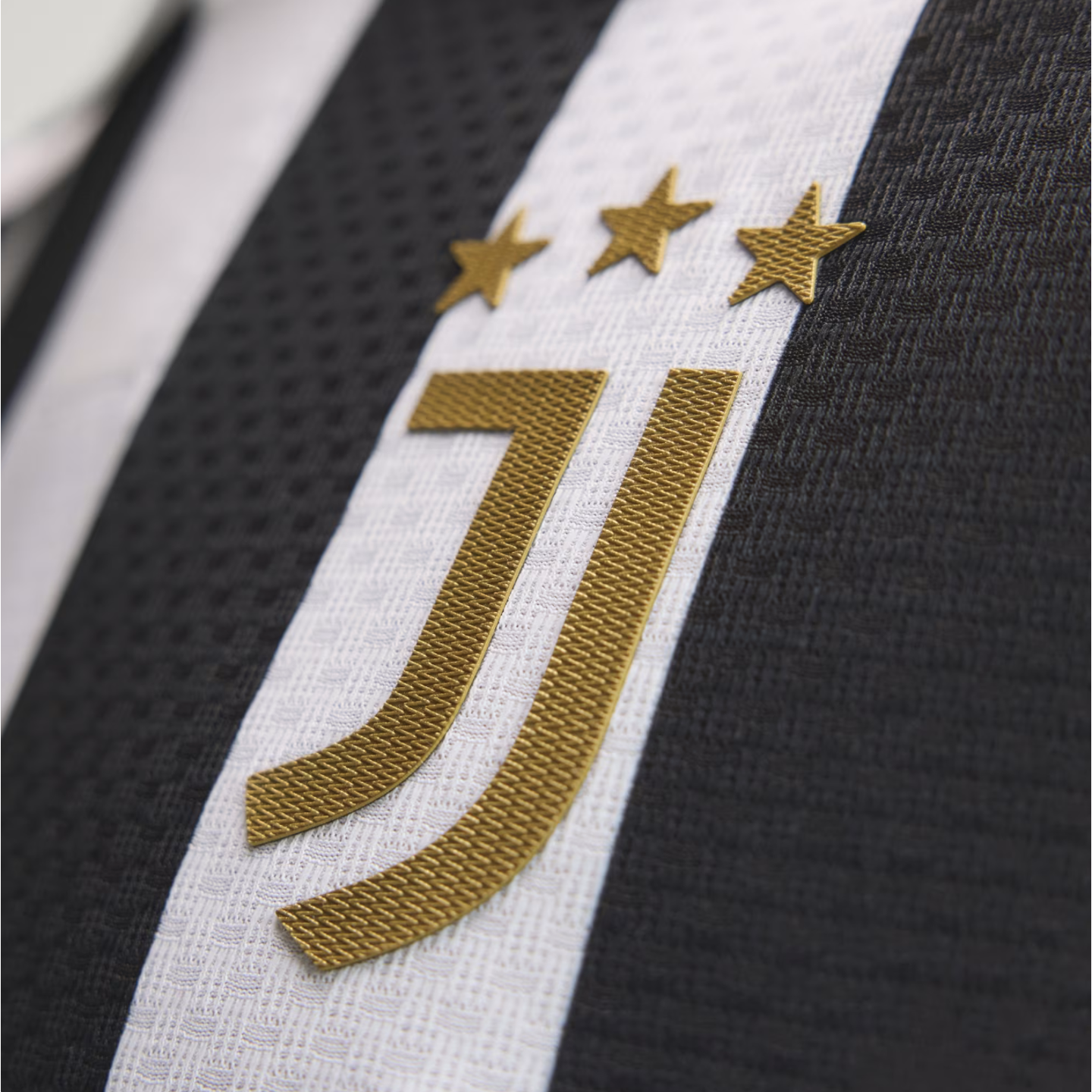 Close-up of the gold Juventus crest and three stars on a black and white striped soccer jersey with textured fabric.