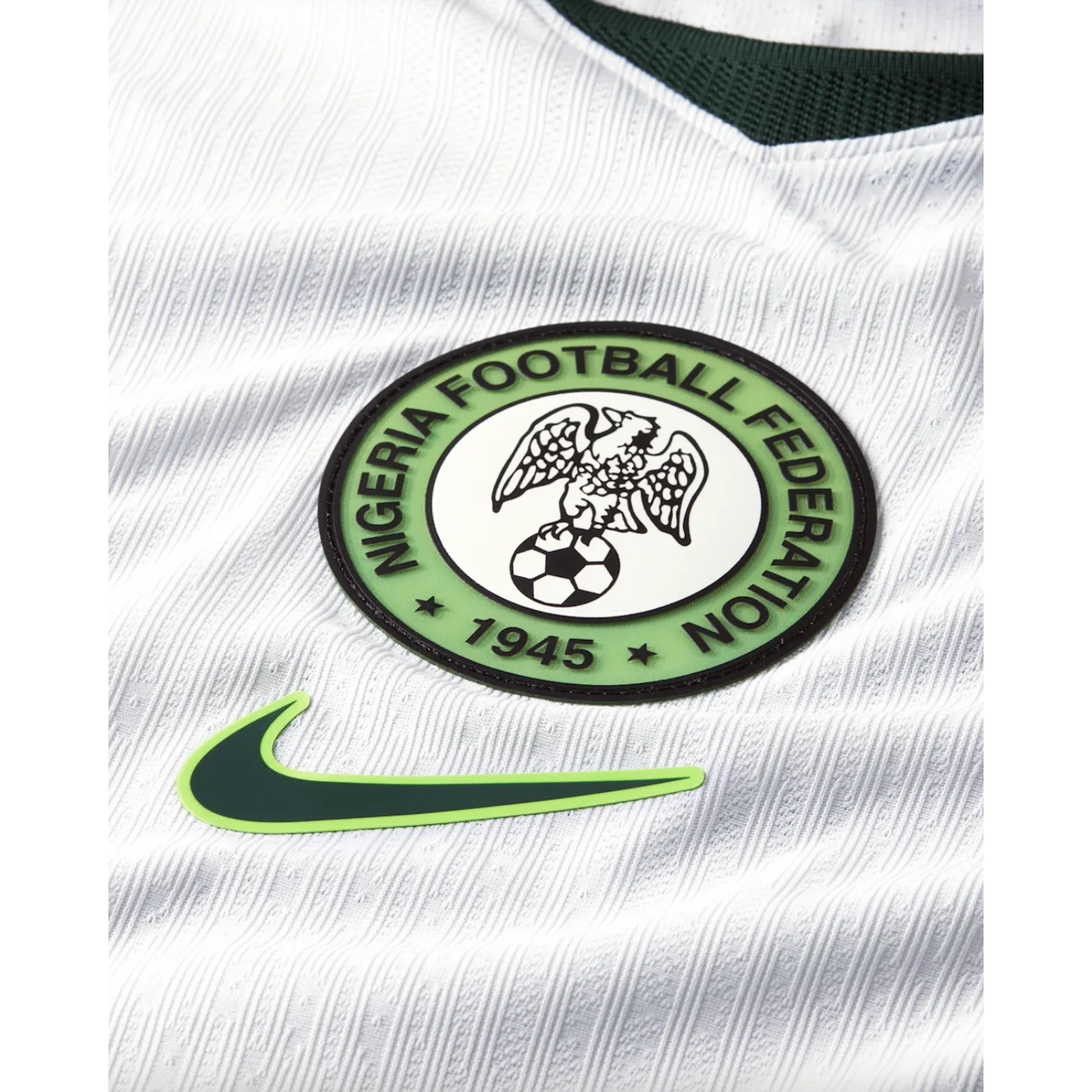 Close-up of a white Nigeria football jersey featuring the Nigeria Football Federation crest and a green Nike swoosh logo on textured, ribbed fabric.