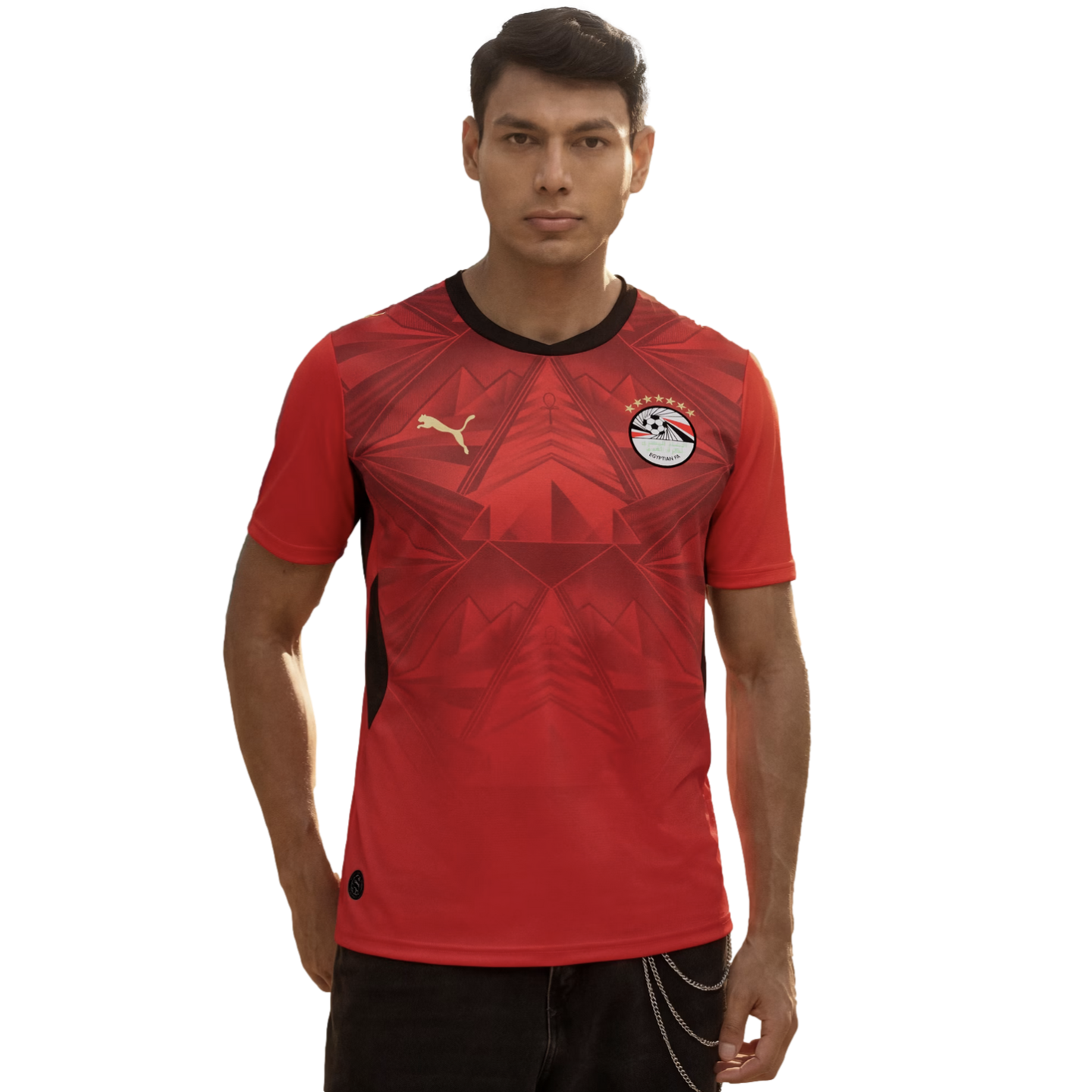 A man wearing a red Egypt national football team home jersey by Puma, featuring subtle geometric patterns and the team crest, standing against a plain black background.