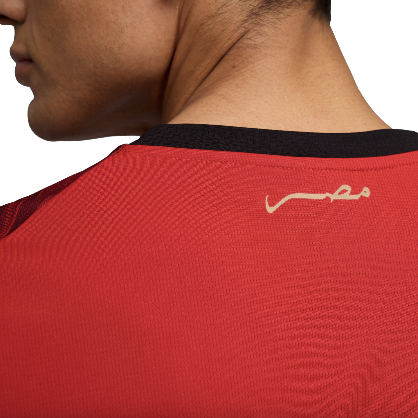 A close-up photograph shows the upper back and neck of a person wearing a red sports jersey. The jersey features a black collar and a stylized gold inscription of the word "Egypt" in Arabic (مصر) on the upper back.