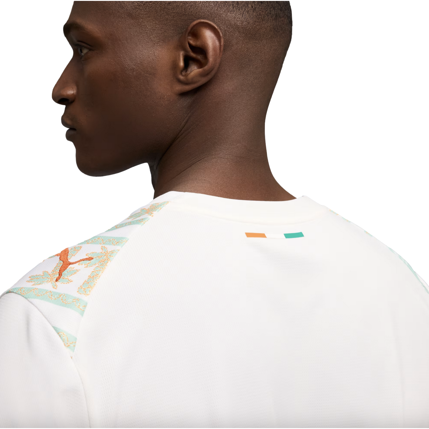 A close-up profile view from the back of a man wearing a white Puma jersey featuring mint green and orange patterned shoulders and a small Ivory Coast flag on the back collar.