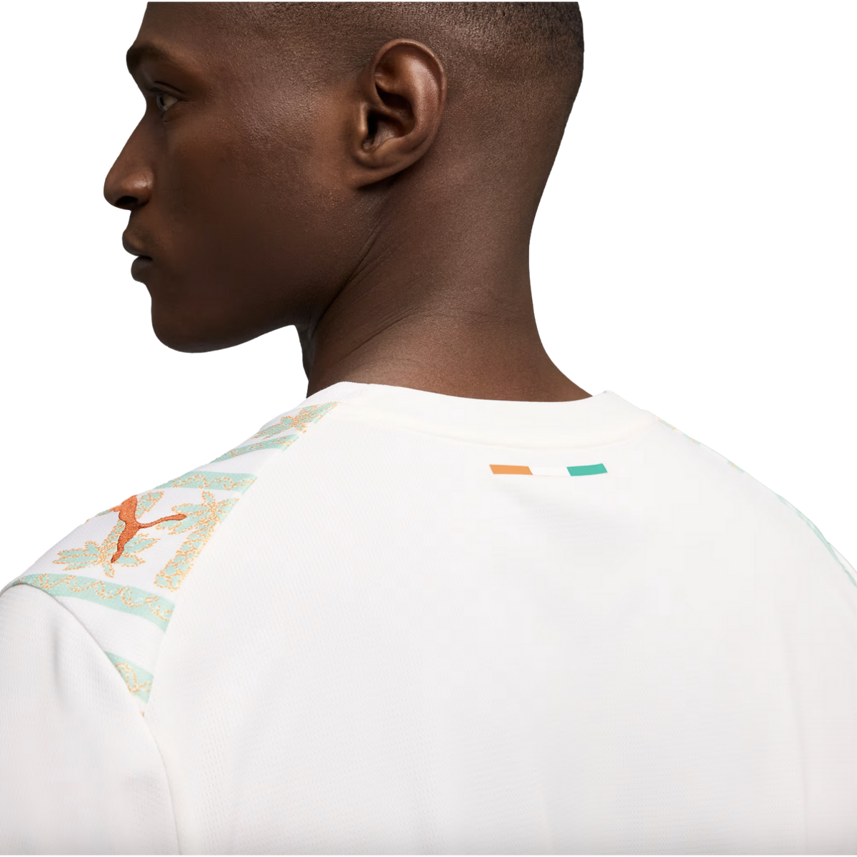 A close-up profile view from the back of a man wearing a white Puma jersey featuring mint green and orange patterned shoulders and a small Ivory Coast flag on the back collar.