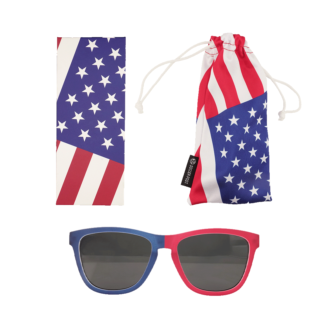 A set of American flag-themed accessories featuring patriotic red, white, and blue colors. The set includes a pair of sunglasses with one blue frame and one red frame, a rectangular cleaning cloth with a star and stripe pattern, and a matching soft drawst
