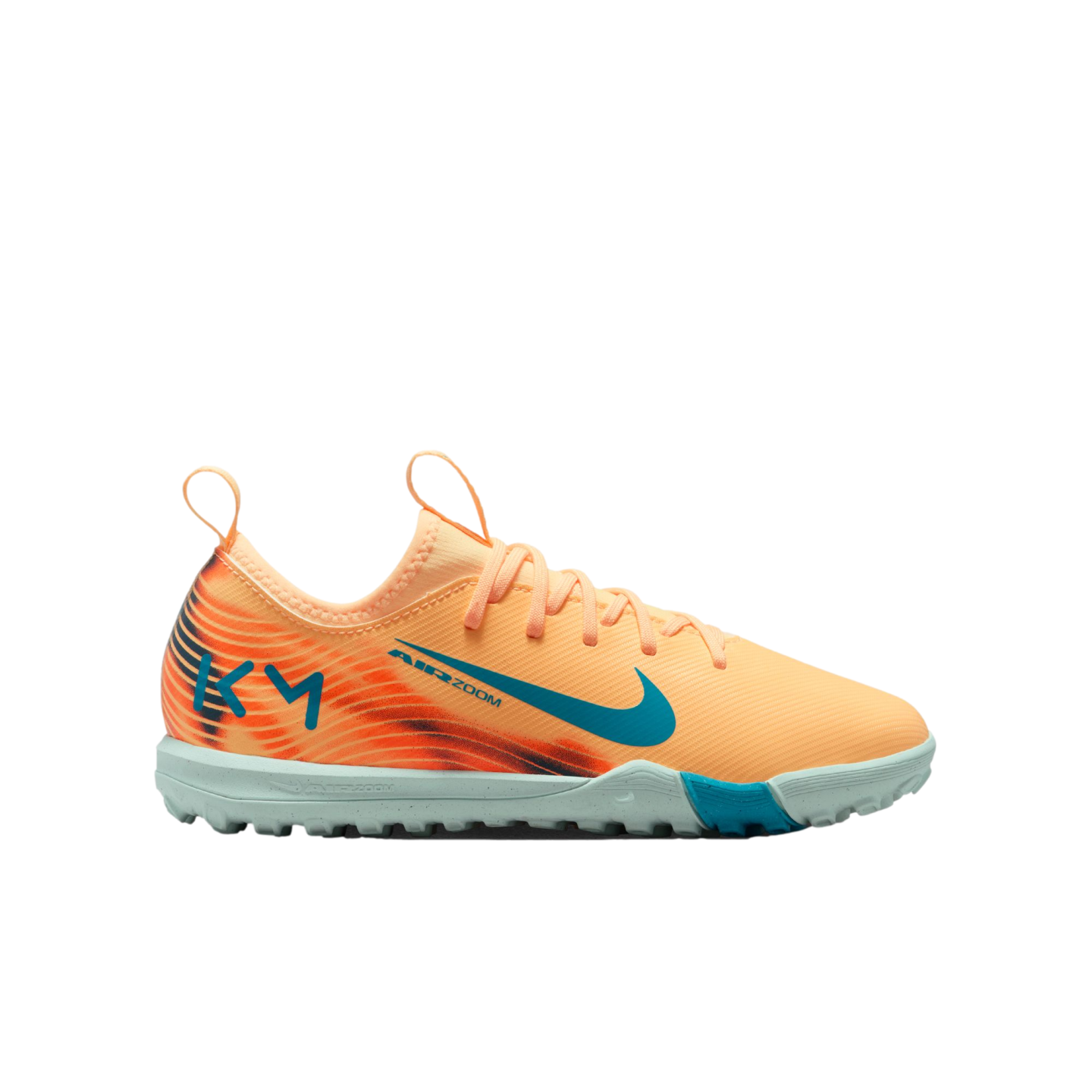 Profile view of a peach Nike turf soccer shoe with teal accents, a light blue sole, and "KM" branding on the heel against a black background.