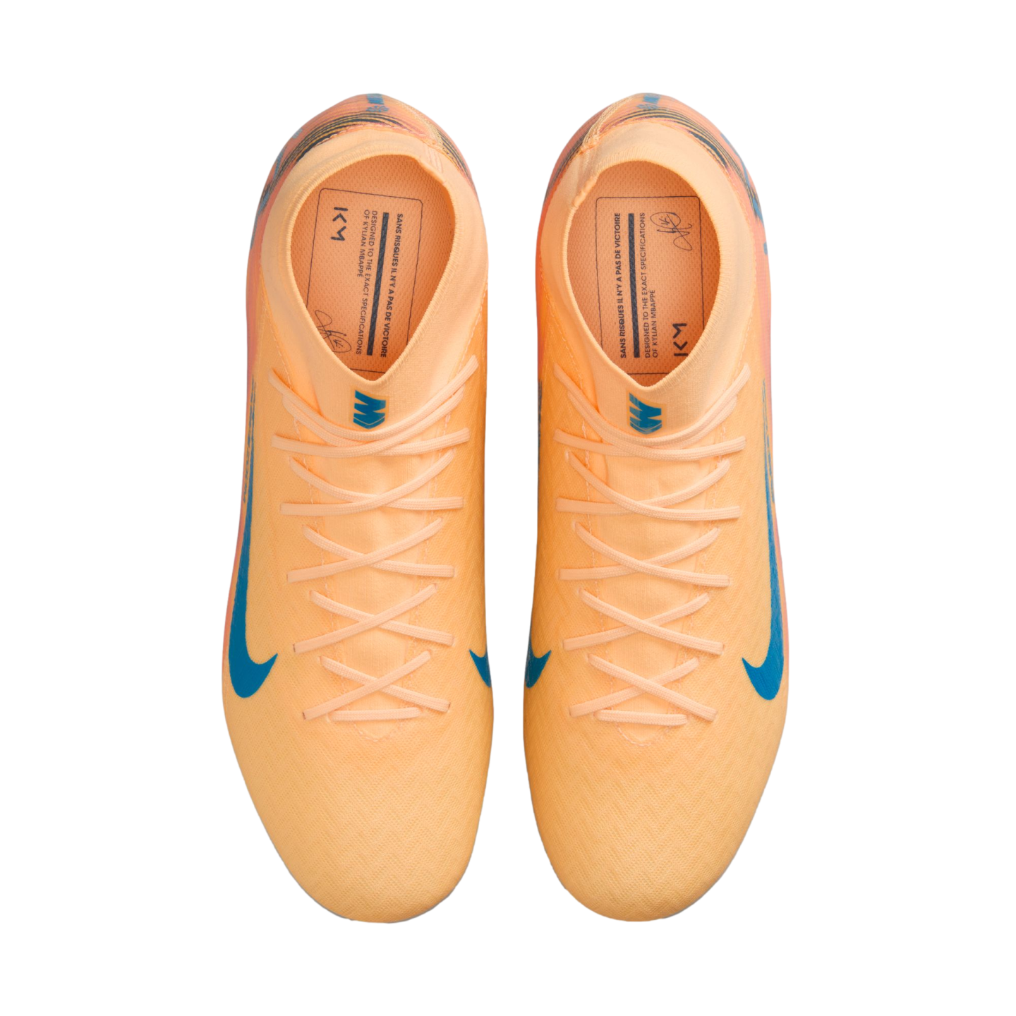 Top-down view of peach Nike Kylian Mbappé soccer cleats with blue accents on a black background.