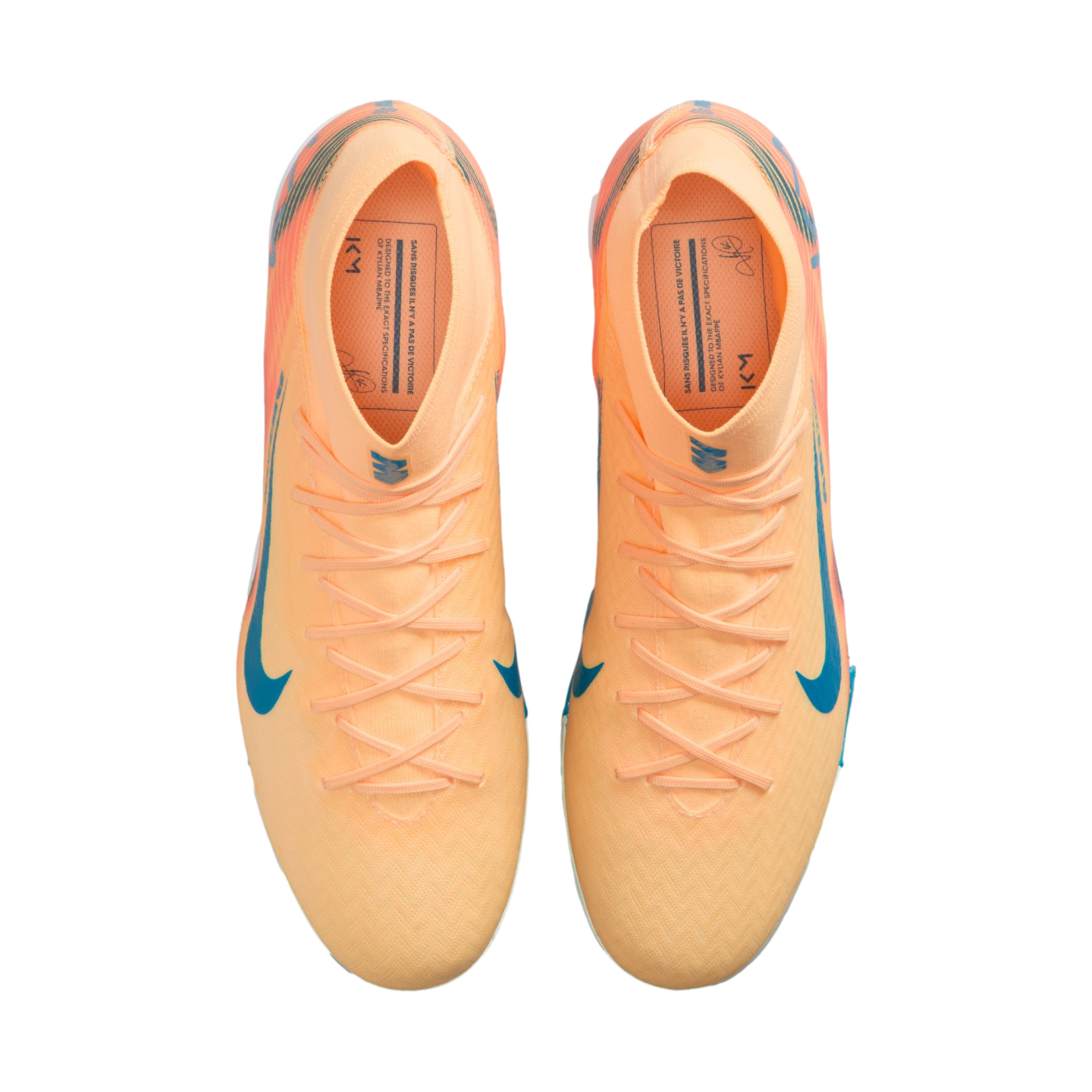 Top-down view of peach-colored Nike soccer cleats with blue swooshes and Kylian Mbappé branding on the insoles, against a black background.