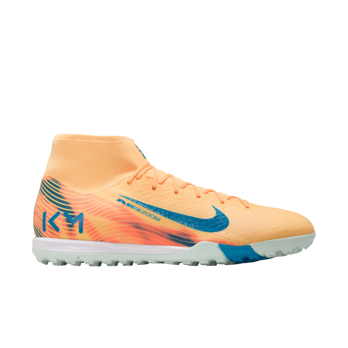 Side profile of a pale orange Nike Mercurial turf soccer shoe with teal accents and Kylian Mbappé's "KM" logo on the heel, set against a black background.