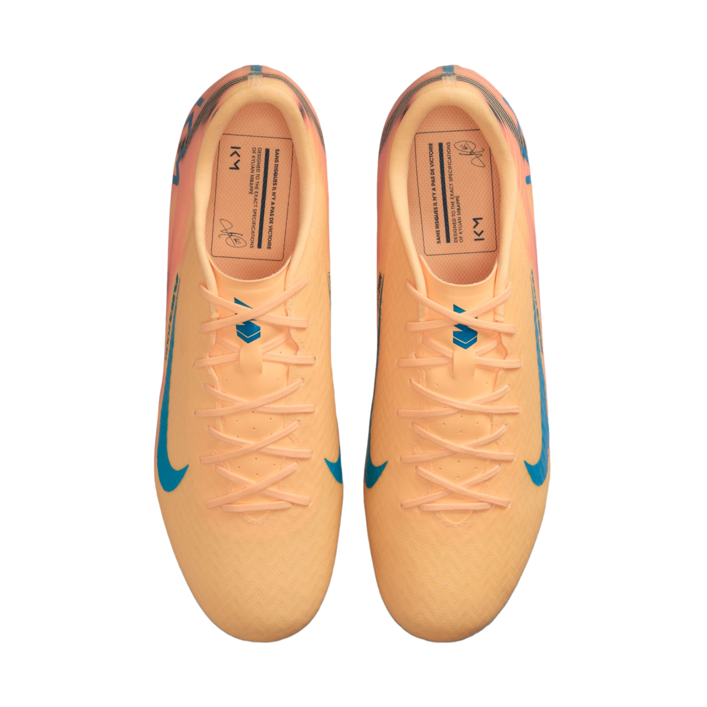 Top-down view of a pair of peach-colored Nike soccer cleats with blue accents and Kylian Mbappé's signature on the insoles.