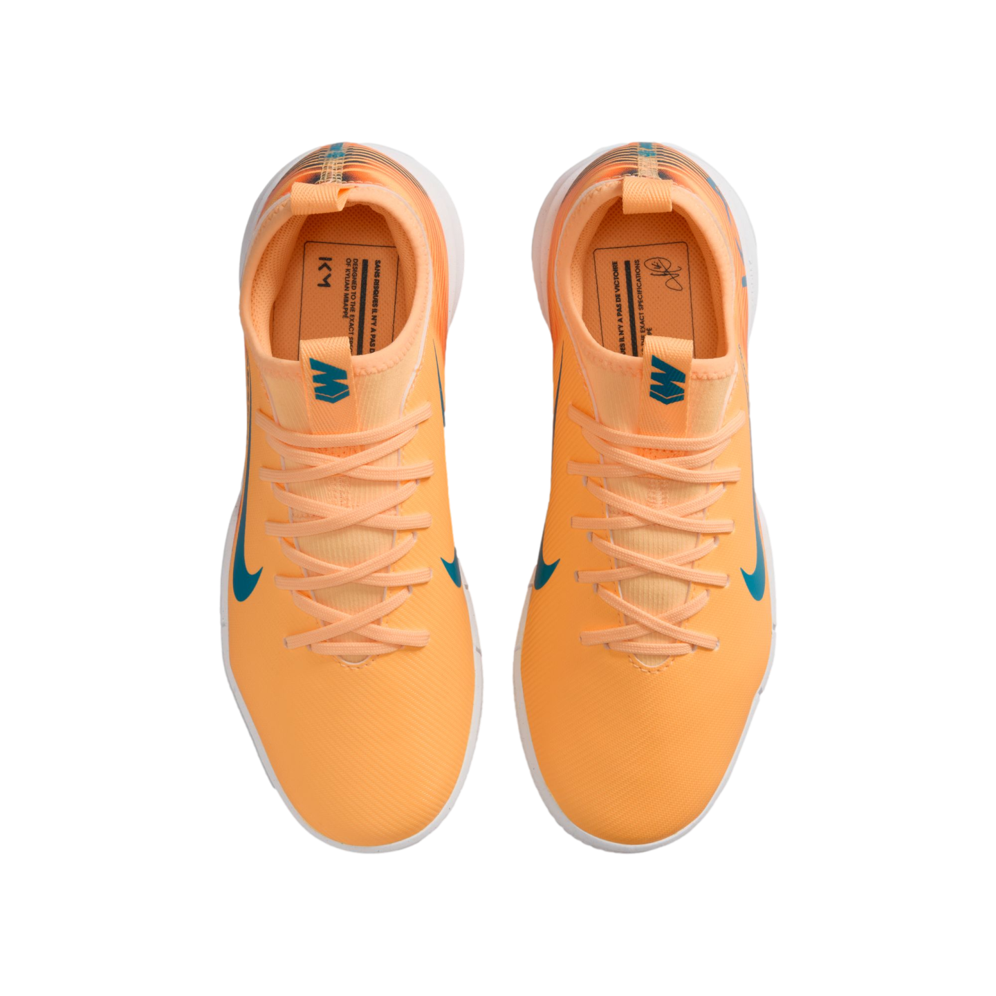 Top-down view of bright orange Nike soccer cleats with teal accents and "KM" branding on the insoles, set against a solid black background.