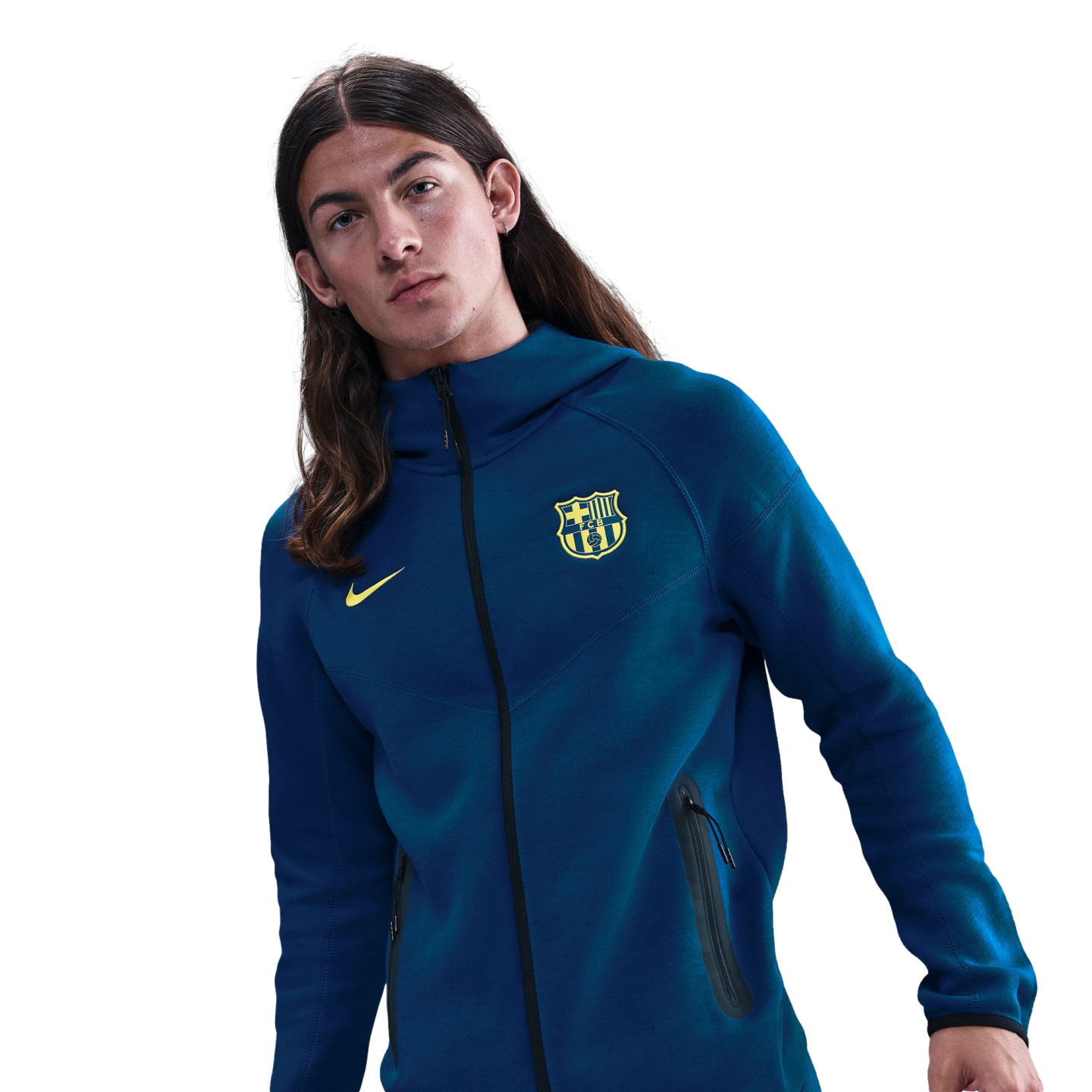 A young man with long brown hair wearing a blue Nike FC Barcelona zip-up hoodie against a black background.