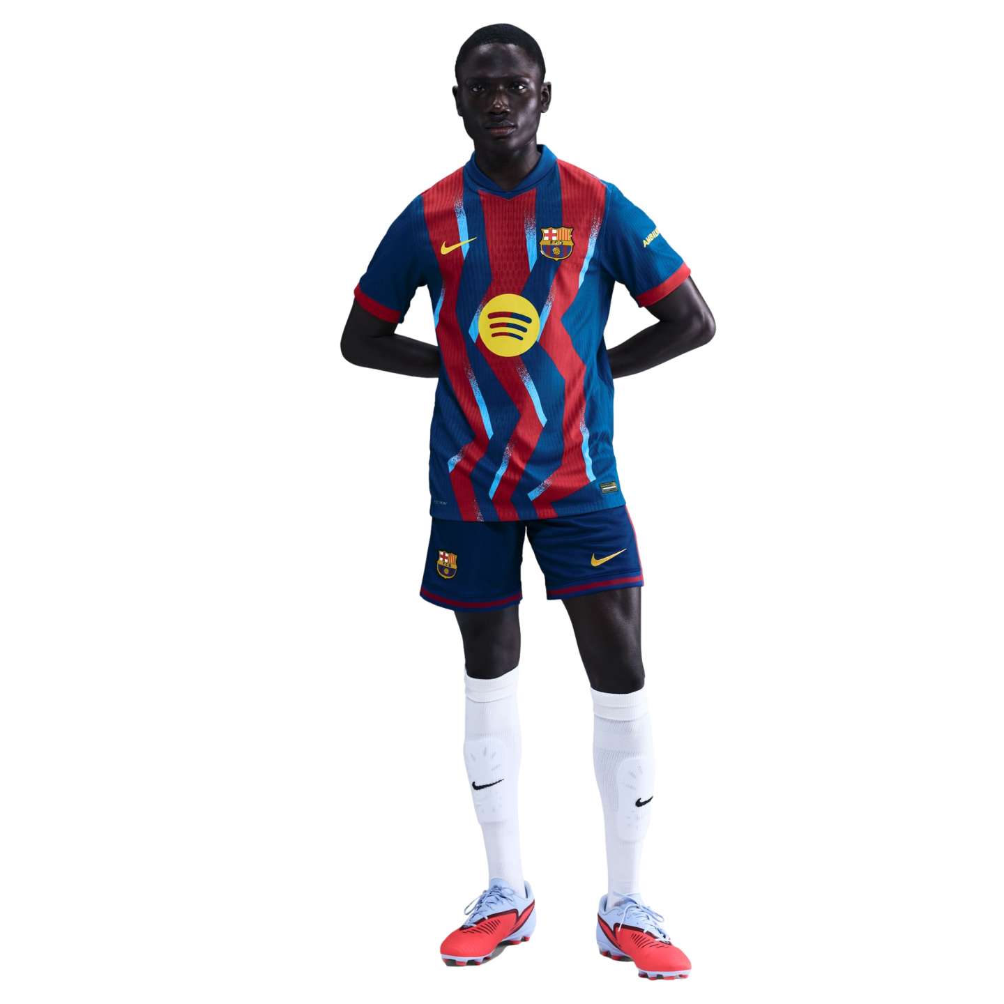 A soccer player models a blue and red patterned FC Barcelona kit with the Spotify logo, white socks, and red cleats against a black background.