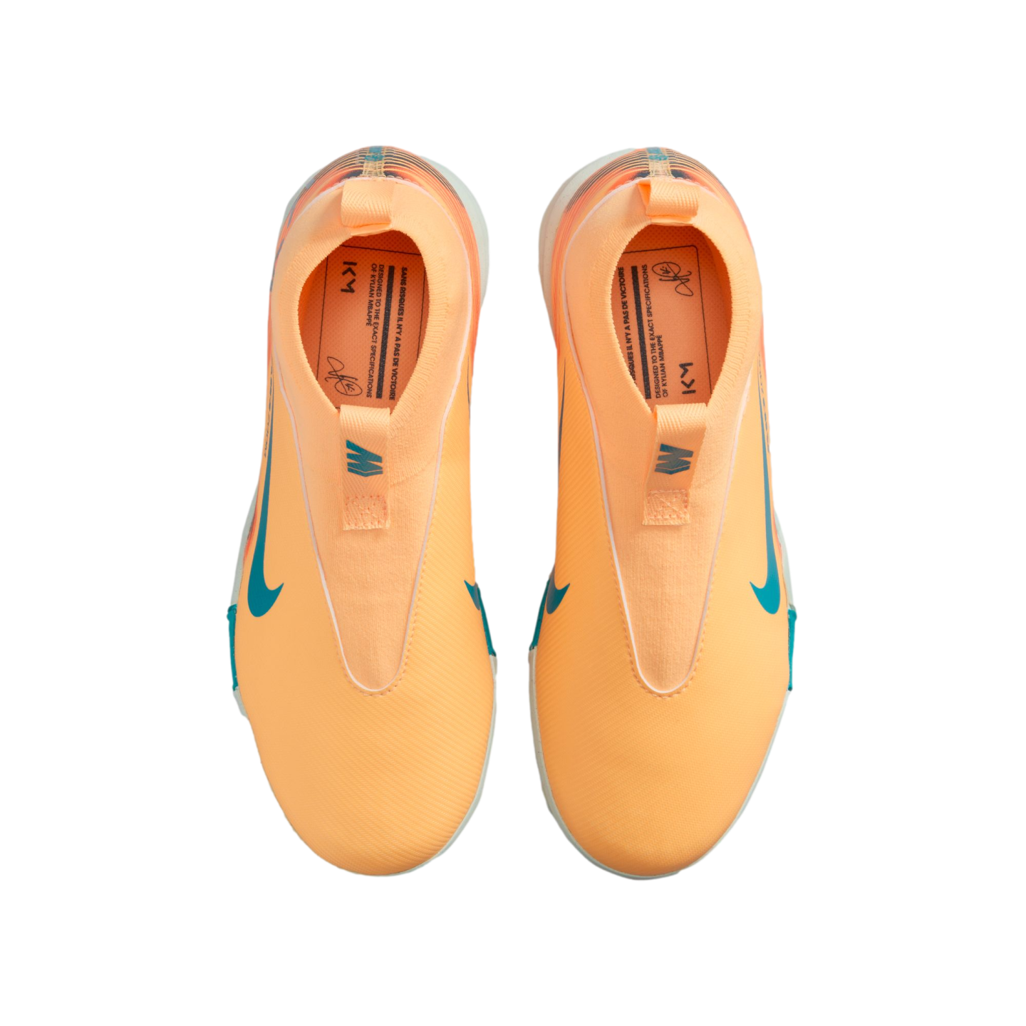 Top-down view of bright orange laceless Nike soccer shoes with teal accents and "KM" branding on the insoles, set against a black background.