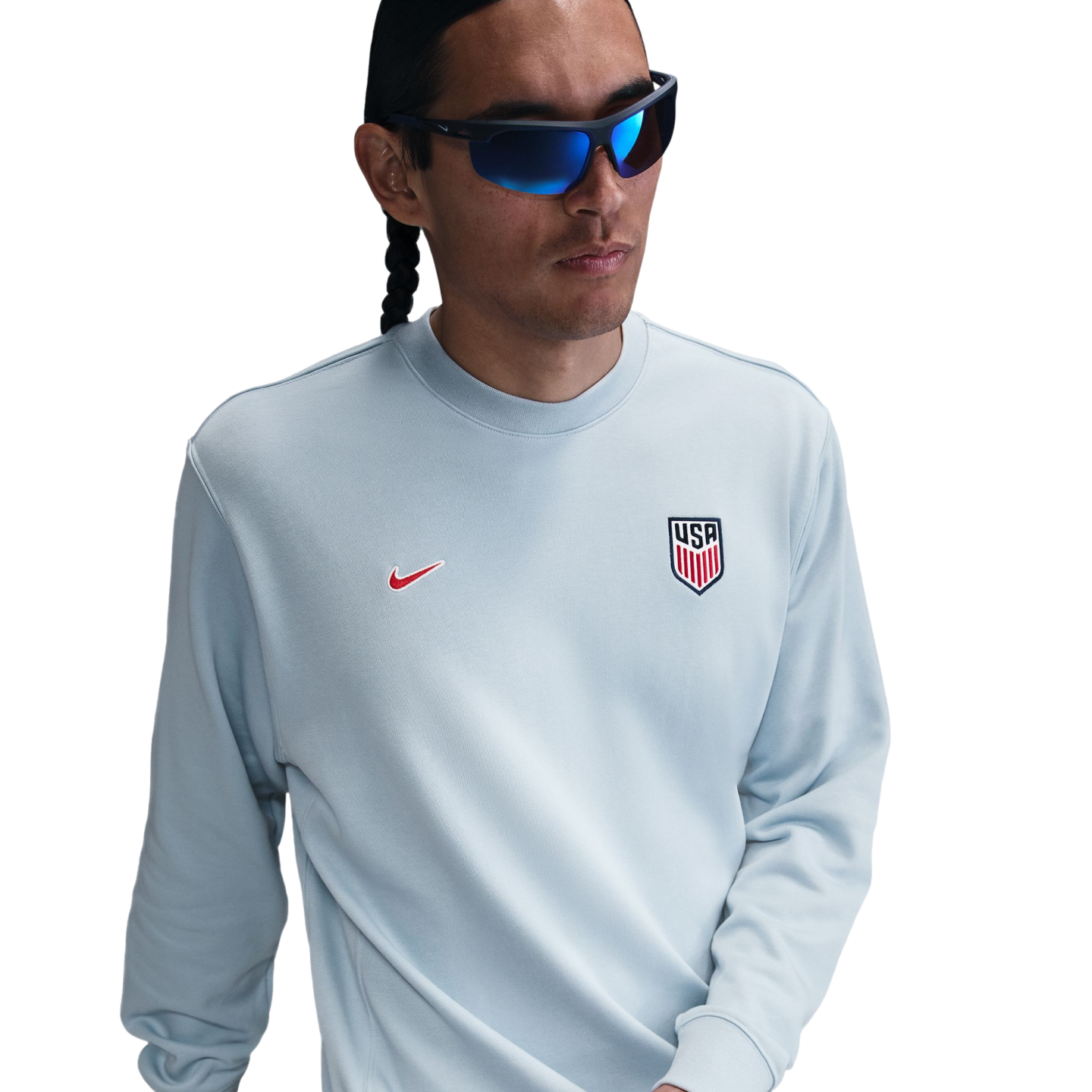 A person wearing blue-tinted wraparound sunglasses and a light blue Nike sweatshirt featuring the USA Soccer crest on the chest.