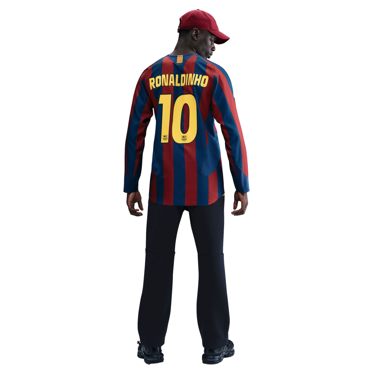 Back view of a man in a Barcelona "Ronaldinho 10" jersey, black pants, and maroon cap, set against a black background.