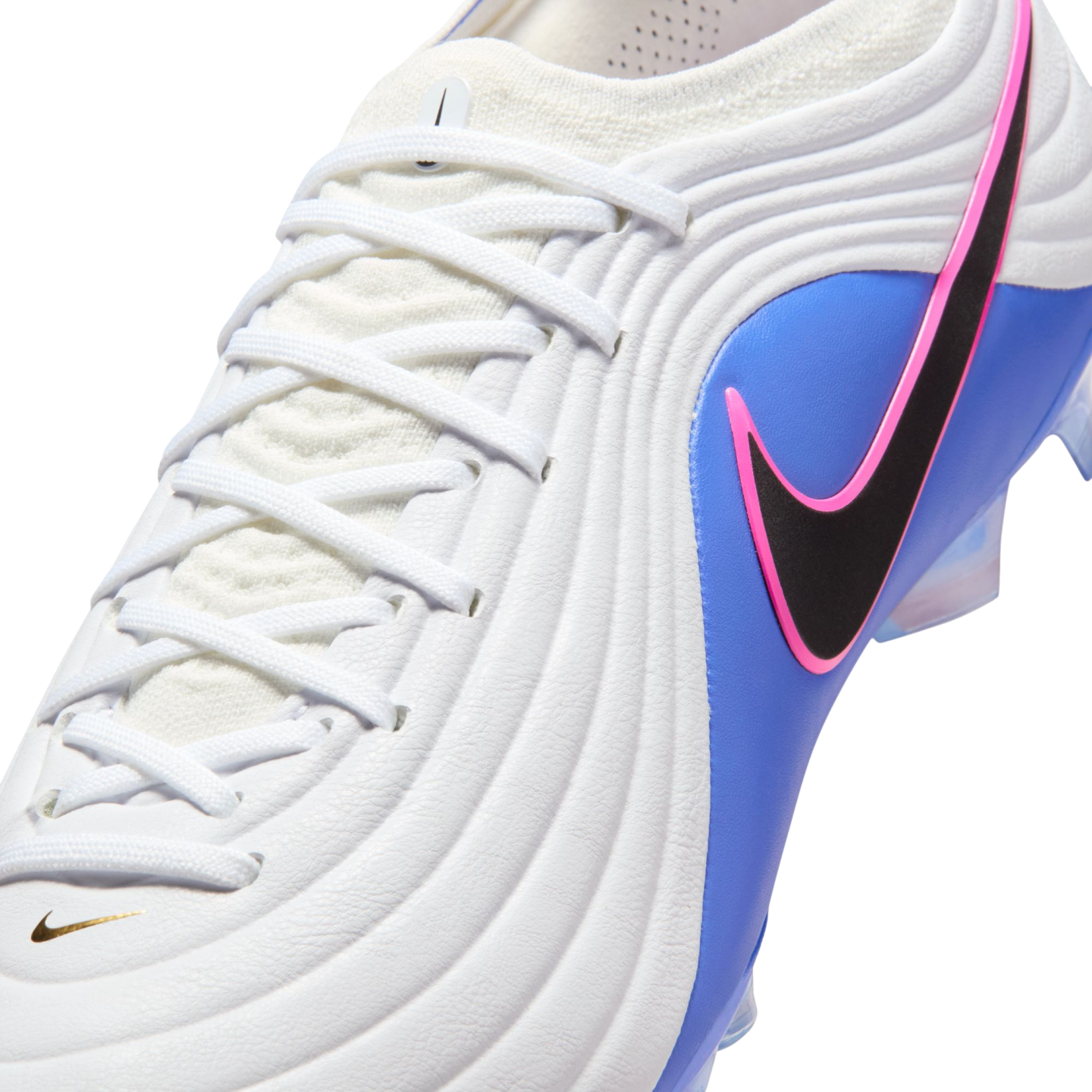 Close-up of a Nike soccer cleat with a white textured upper, blue side panel, and a black swoosh outlined in pink. Features white laces and a small gold swoosh.