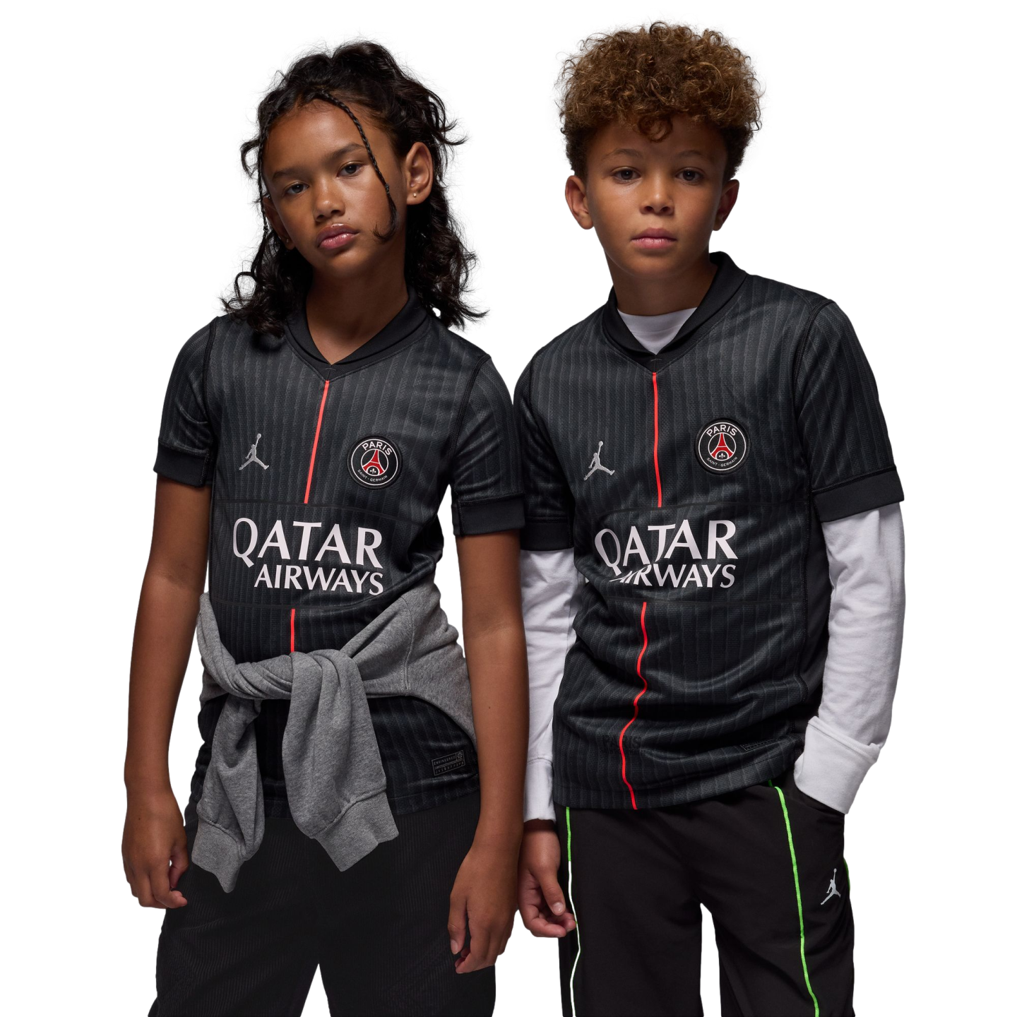 A young girl and boy wear matching black Paris Saint-Germain soccer jerseys with red vertical stripes and logos while posing against a solid black background.