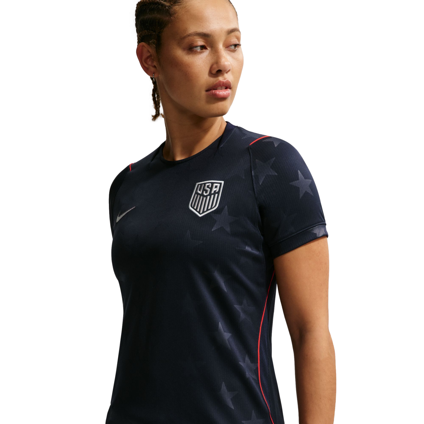 A woman in a navy blue USA soccer jersey with subtle star patterns and a white team crest, looking to her right against a black background.