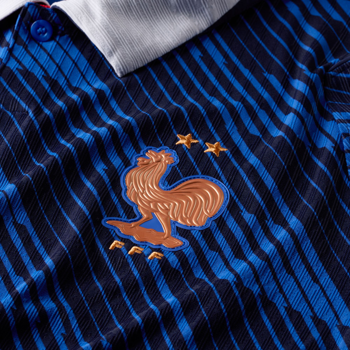 Close-up of a blue and black striped France football jersey featuring the golden Gallic rooster crest with two stars and "FFF" lettering.