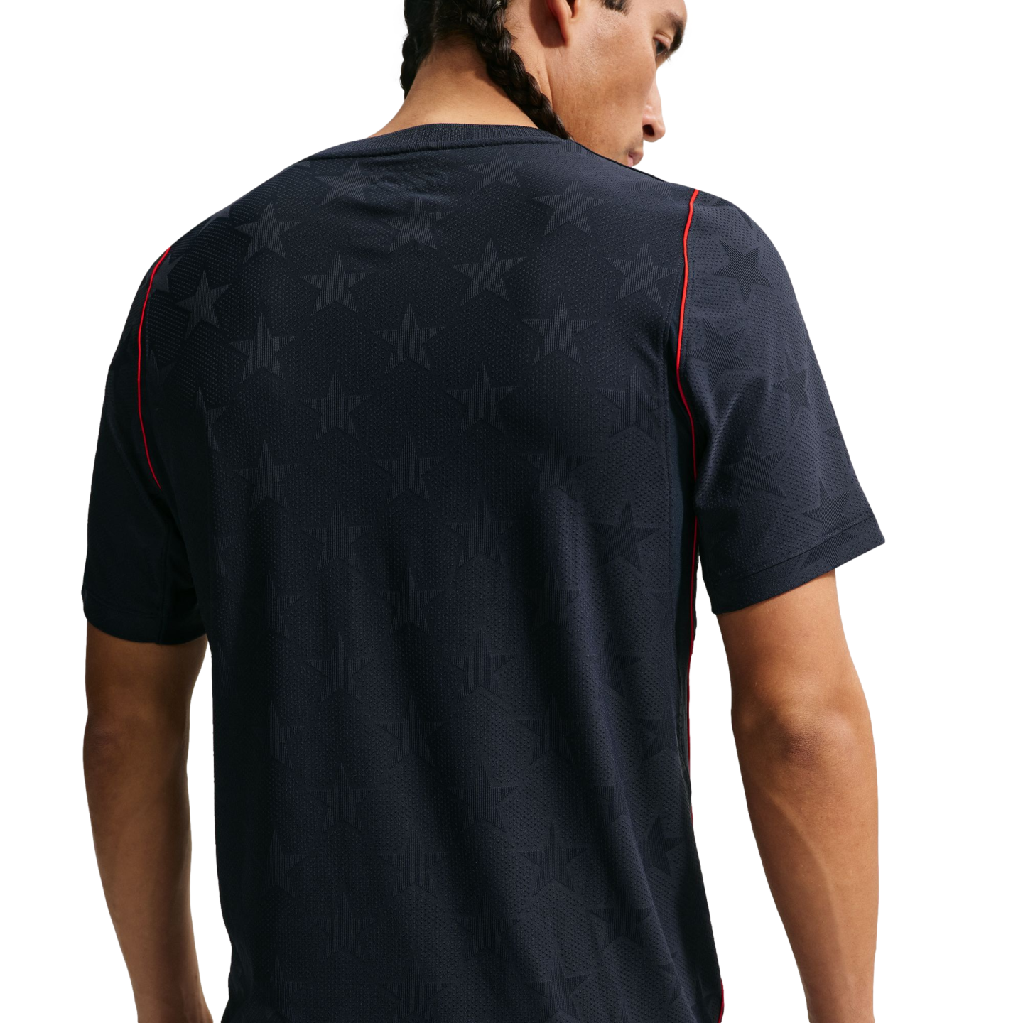 Back view of a man with braided hair wearing a dark navy t-shirt featuring a subtle star pattern and red piping on the shoulders, set against a plain black background.