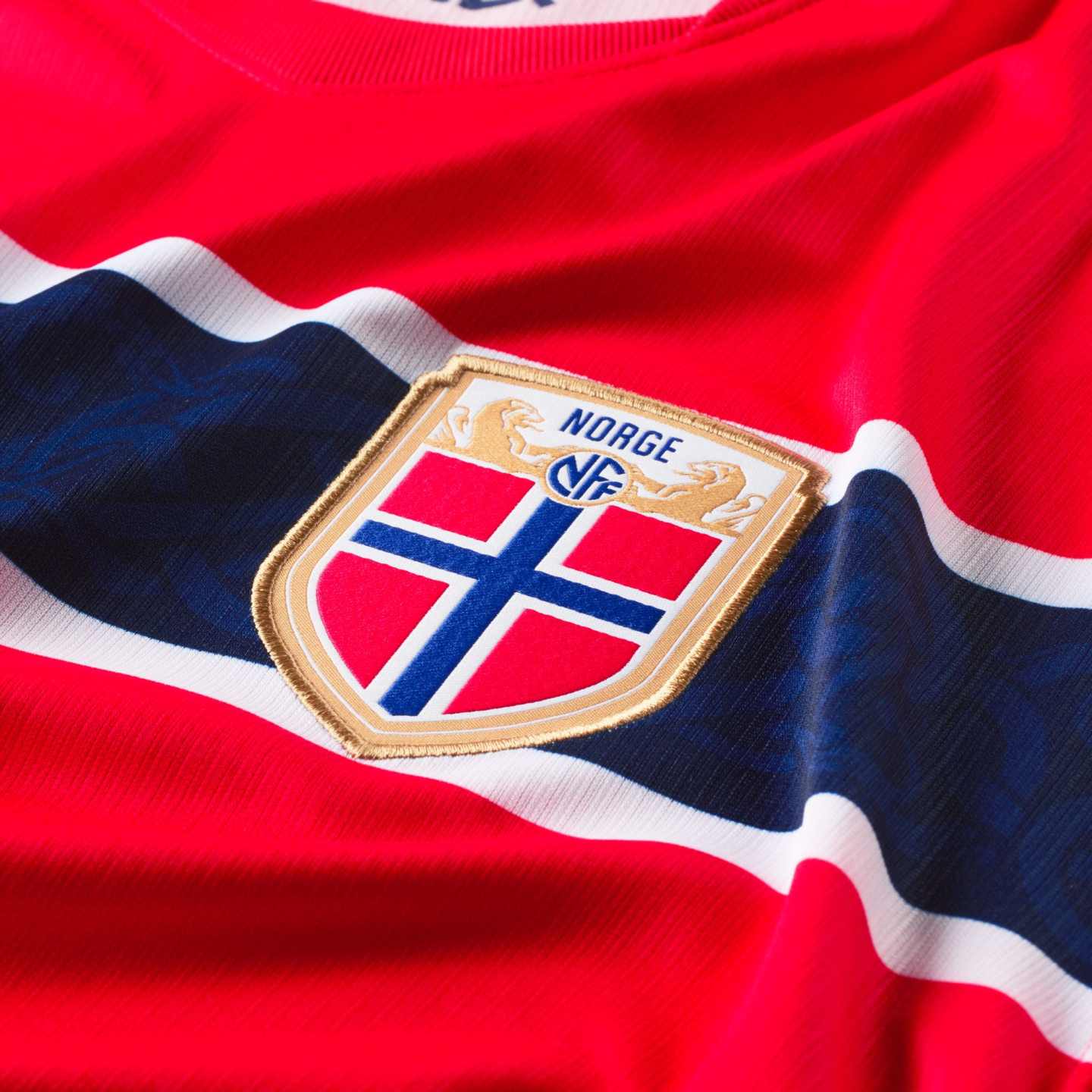 Close-up of a red Norway national football jersey with a central crest featuring the Norwegian flag and "NORGE" text over a horizontal blue band with white borders.