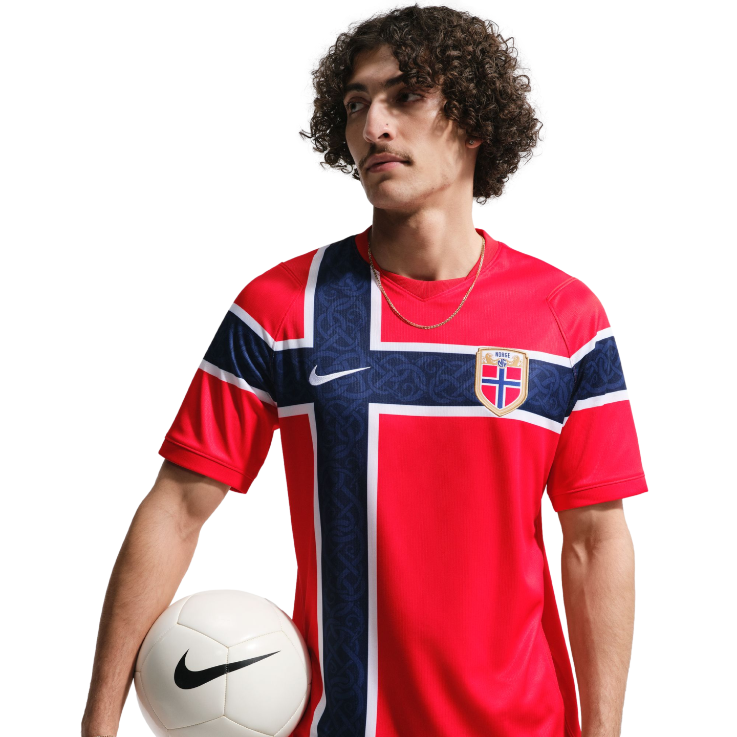 Man with curly hair wearing a red Norway national team soccer jersey and holding a white soccer ball against a black background.