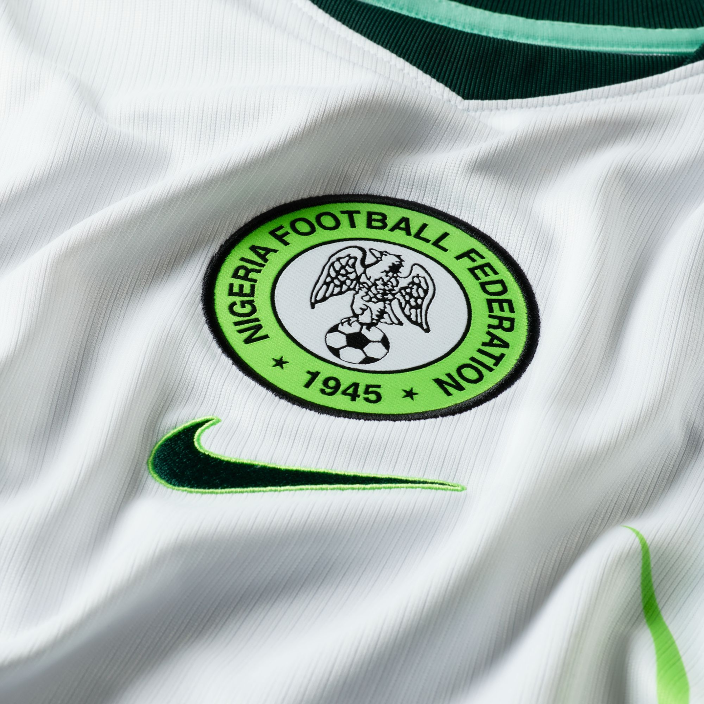 Close-up of a white Nike Nigeria football jersey featuring the circular Nigeria Football Federation crest and a green Nike swoosh logo against ribbed white fabric.