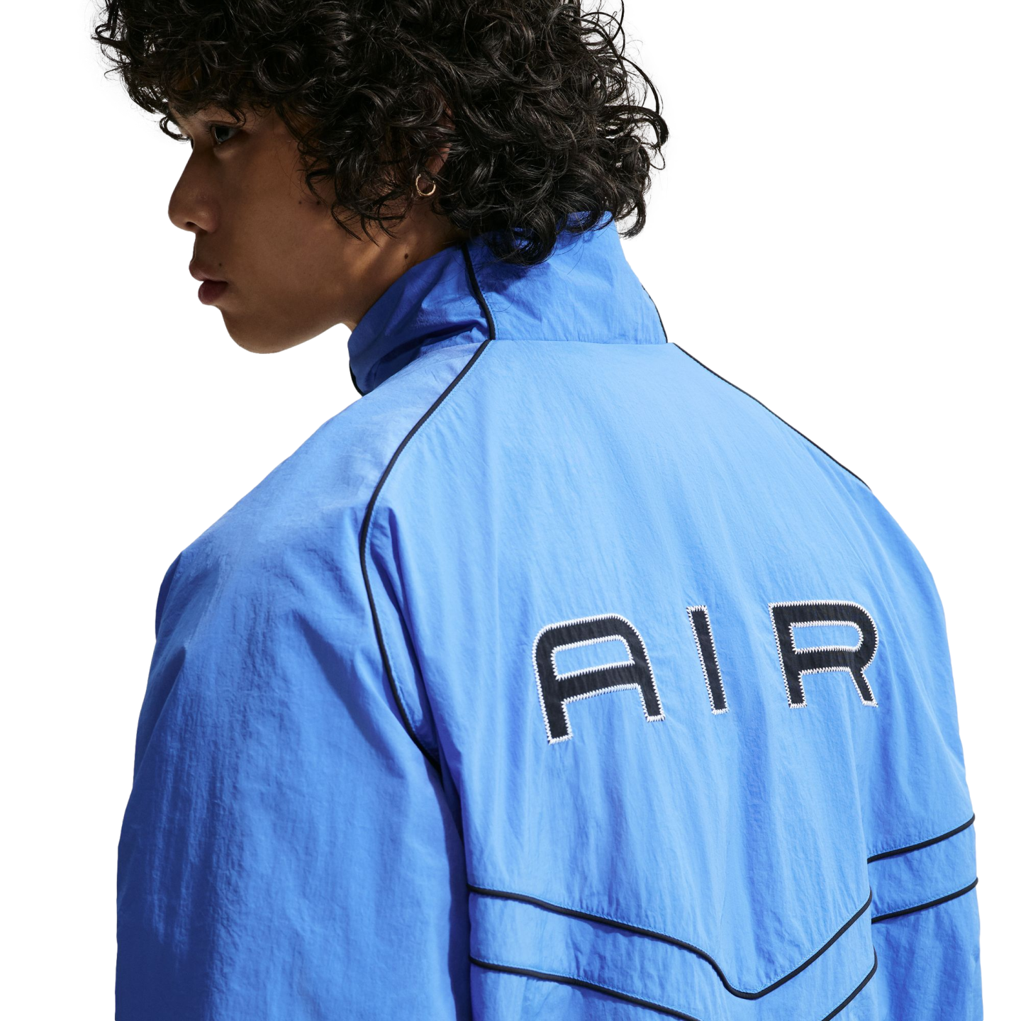 A person with curly dark hair seen from behind, wearing a light blue zip-up jacket with "AIR" printed in black on the back and black piping details.
