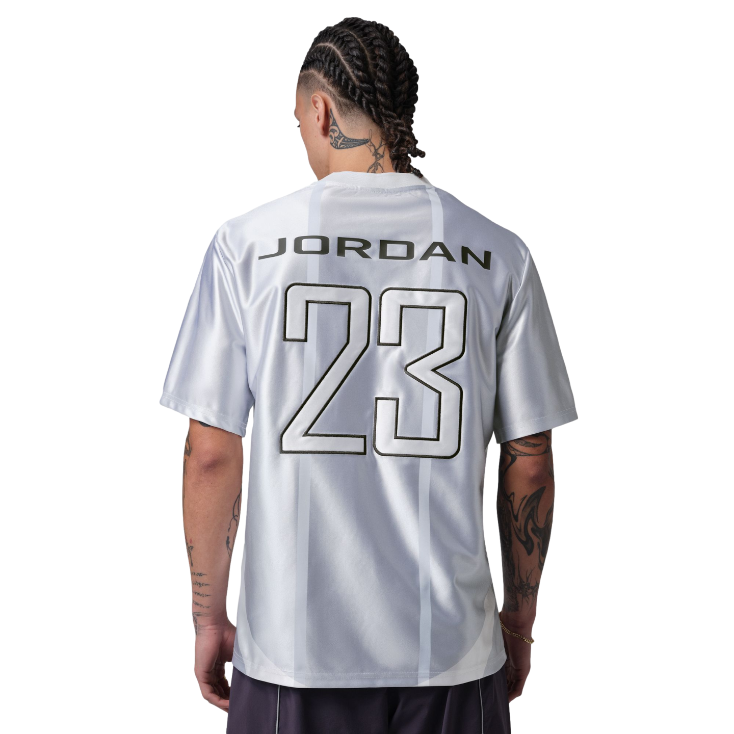 A person with braided hair and tattoos stands with their back to the camera, wearing a silver jersey with "JORDAN 23" printed on the back against a black background.