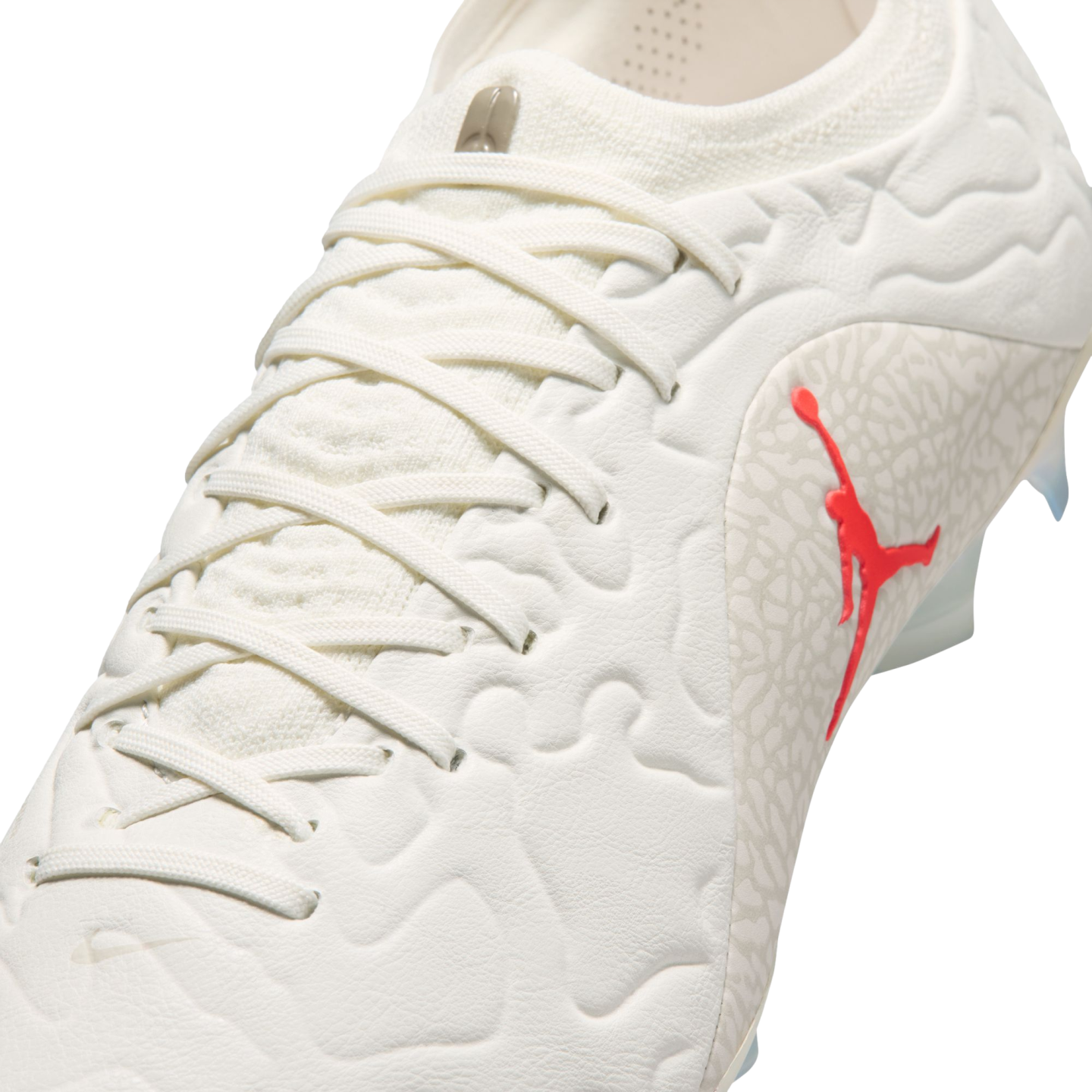 Close-up of a white Jordan Brand soccer cleat with a red Jumpman logo and grey elephant print pattern on the side.