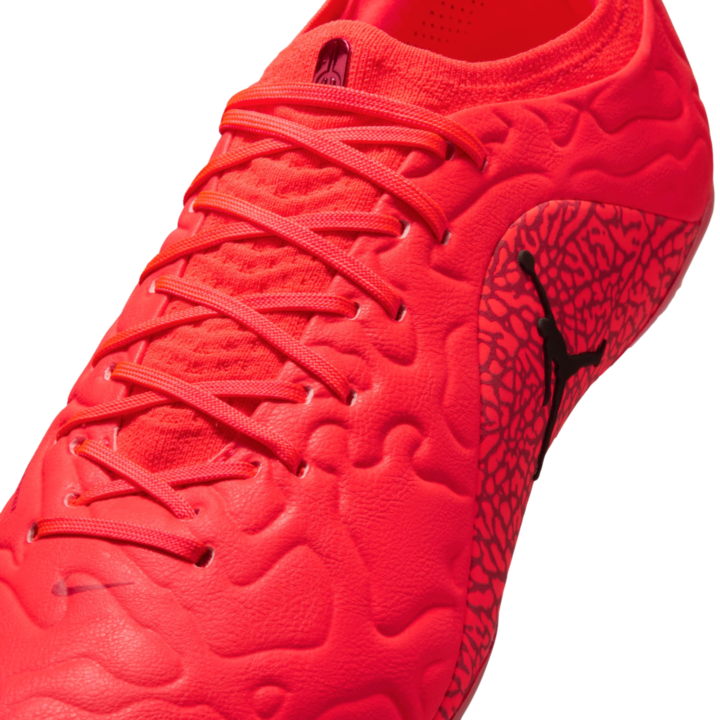 Close-up of a bright red soccer cleat with matching laces, a textured upper, and a black Jumpman logo on the side against a black background.