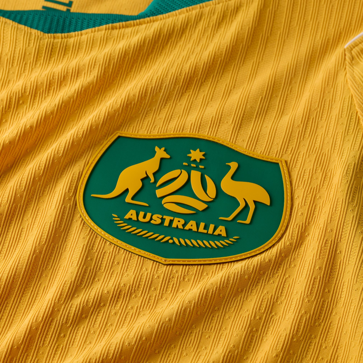 Close-up of a yellow textured sports jersey with a green crest featuring a yellow kangaroo, emu, and the word "AUSTRALIA".