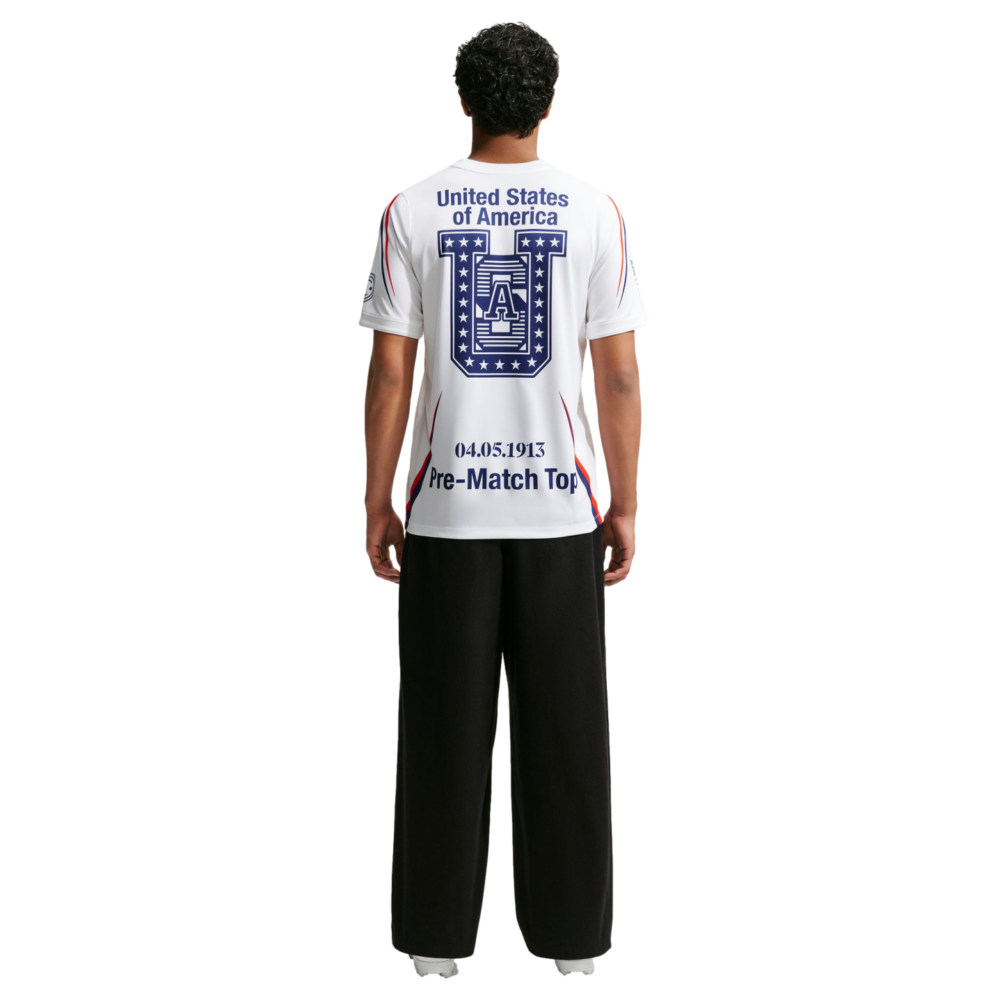 Rear view of a person wearing a white t-shirt with "United States of America" and a large blue logo on the back, paired with black wide-leg trousers.