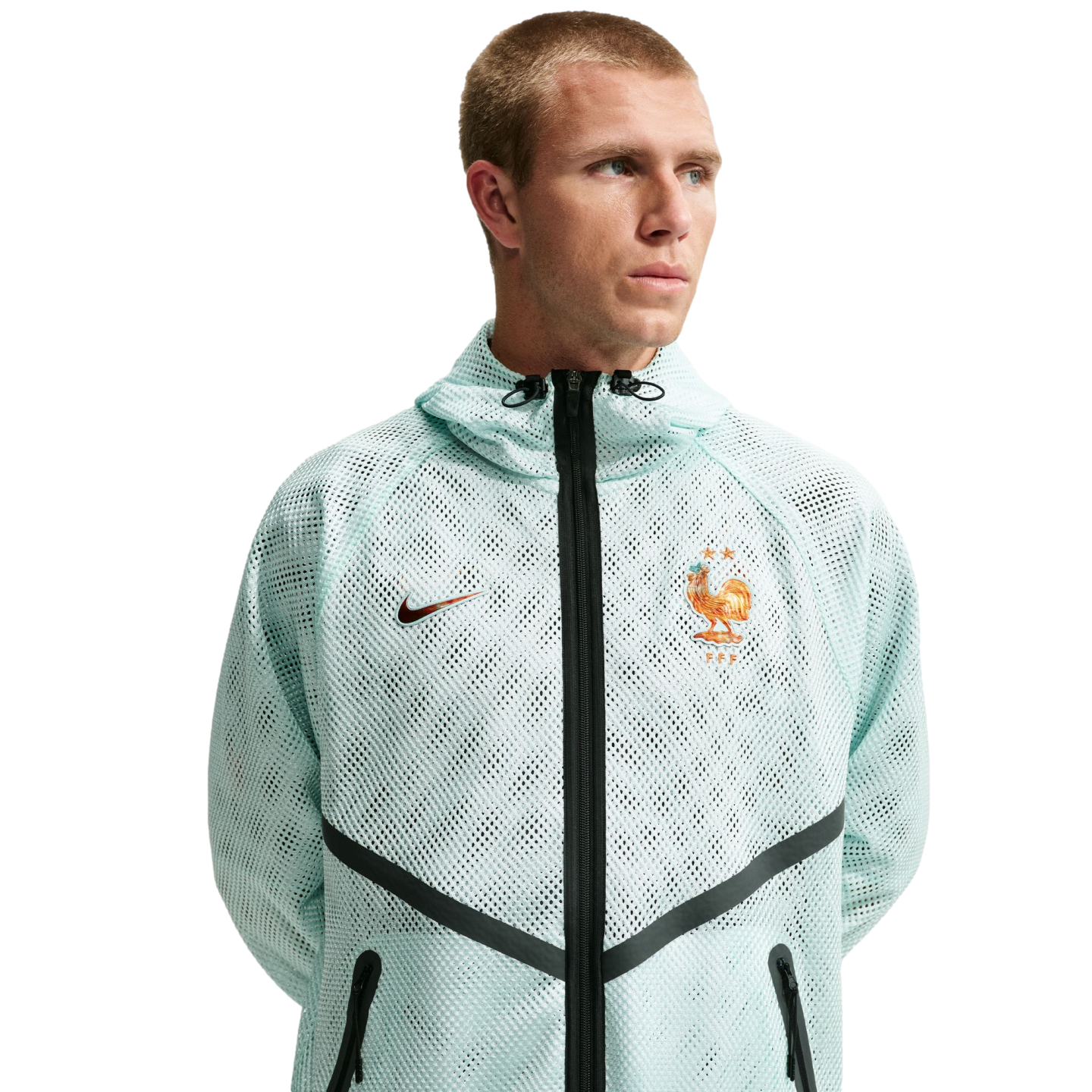 A man wearing a light mint green, mesh Nike zip-up hoodie with the French Football Federation (FFF) crest and black chevron detailing, set against a solid black background.