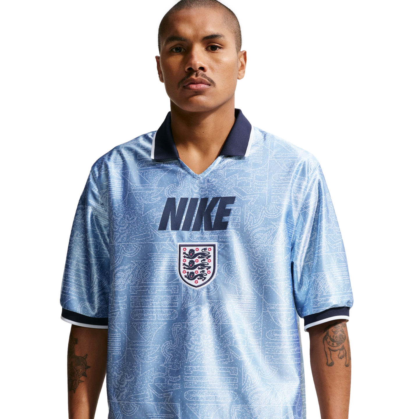A man wearing a light blue, patterned Nike England football jersey with a navy blue collar and the Three Lions crest, posed against a white background.