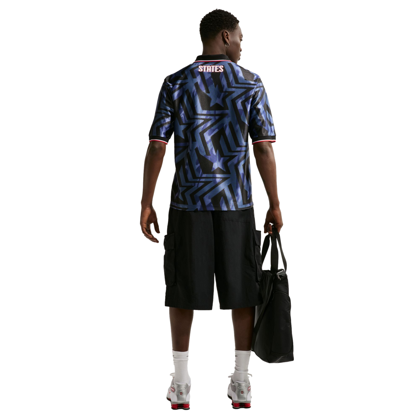 Rear view of a man wearing a blue star-patterned jersey with "STATES" on the back, black shorts, and silver sneakers, holding a black bag.