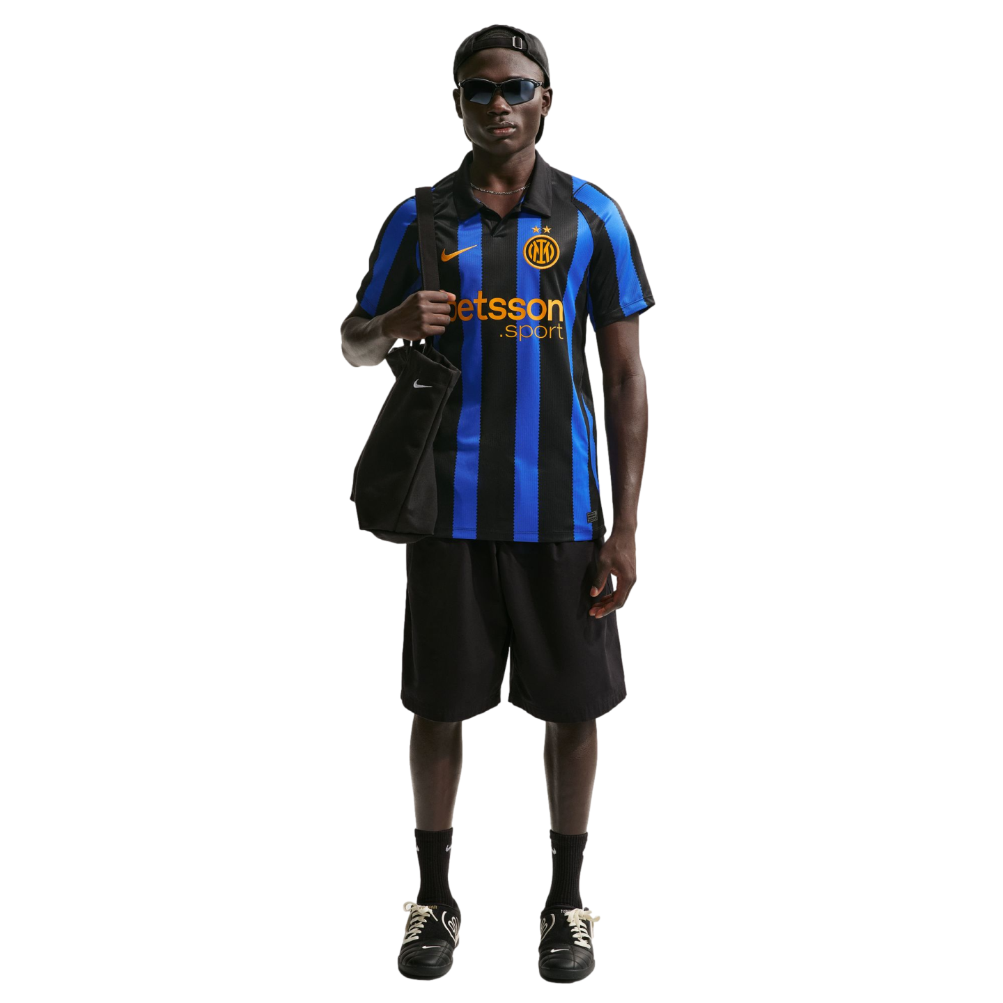 A Black man models an Inter Milan soccer jersey, black shorts, and sunglasses, carrying a black tote bag against a white background.