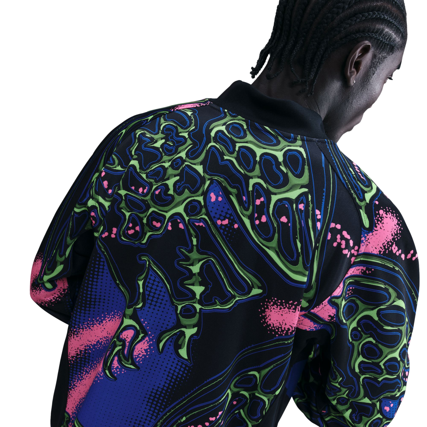 Rear view of a person with braided hair wearing a black jacket with a vibrant neon green, pink, and blue abstract skeletal pattern.