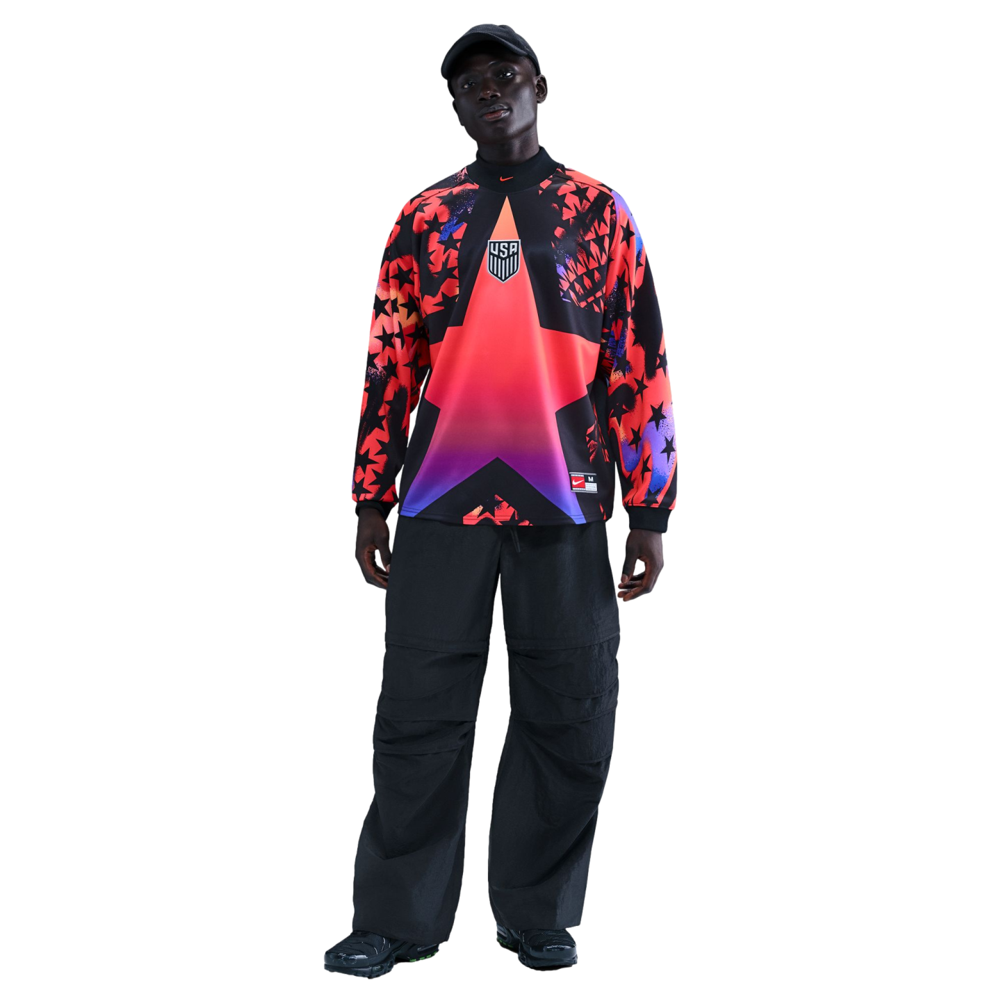 A person models a vibrant USA long-sleeve jersey with a large star design and baggy black pants against a black background.
