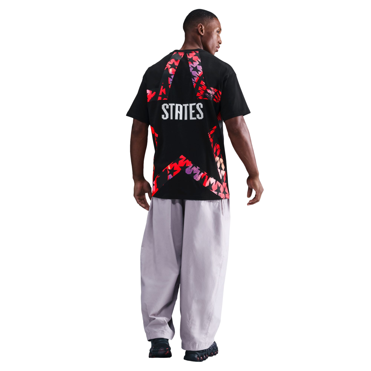 Rear view of a man wearing a black t-shirt with a large red star graphic and "STATES" text, paired with baggy light-colored pants against a black background.