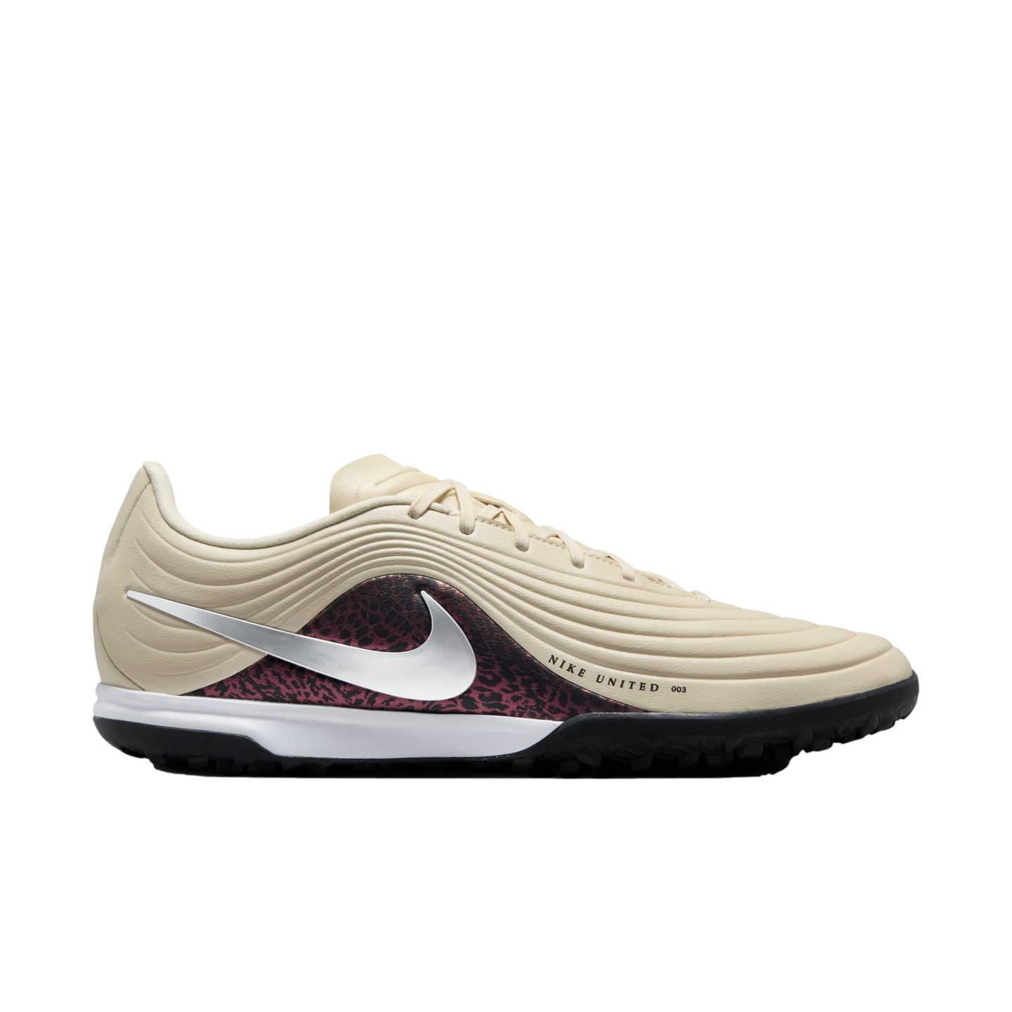 A profile view of a beige Nike United turf soccer shoe featuring a silver swoosh and maroon patterned accents on a black background.