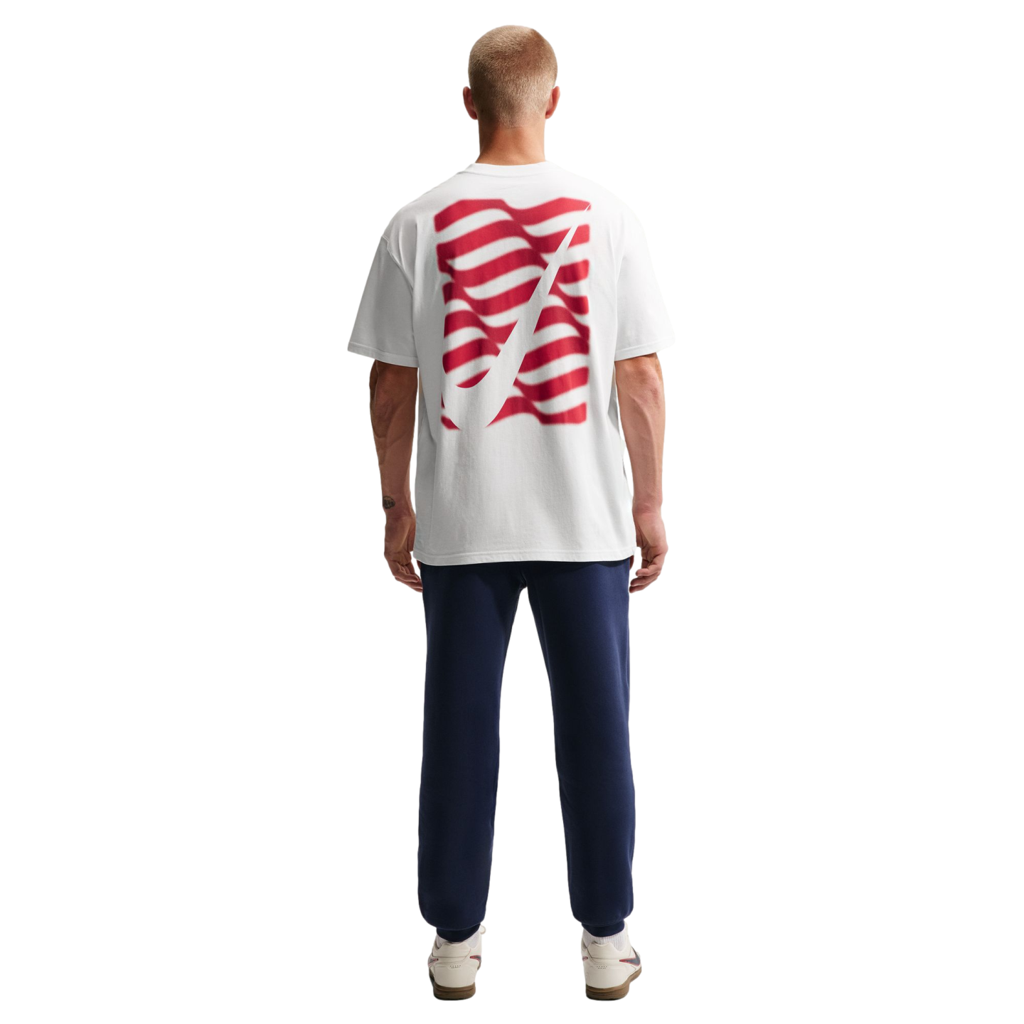 Rear view of a man wearing a white t-shirt with a red wavy graphic, navy blue sweatpants, and white sneakers against a solid black background.