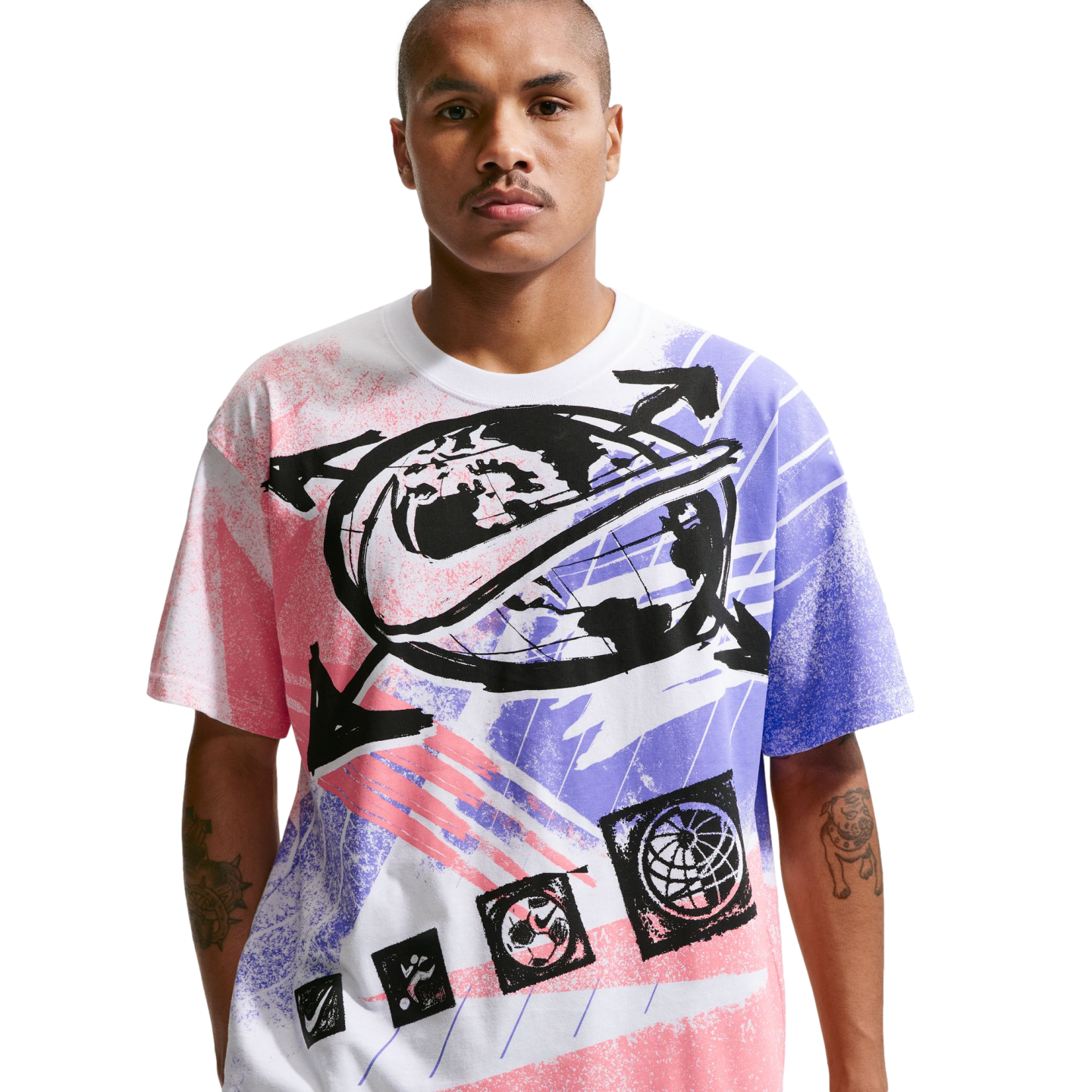 A man with short hair and a mustache stands against a solid black background, wearing a white t-shirt with a large, colorful Nike graphic. The graphic includes a central globe design with a black swoosh, surrounded by arrows and spray-paint style patterns