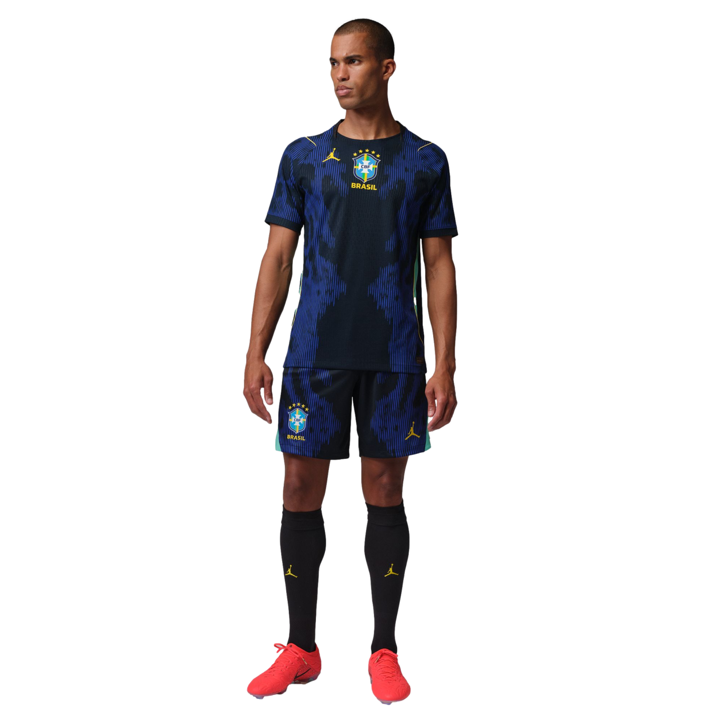 A man wearing a blue and black Brazil soccer kit with yellow Jordan logos and red cleats against a black background.