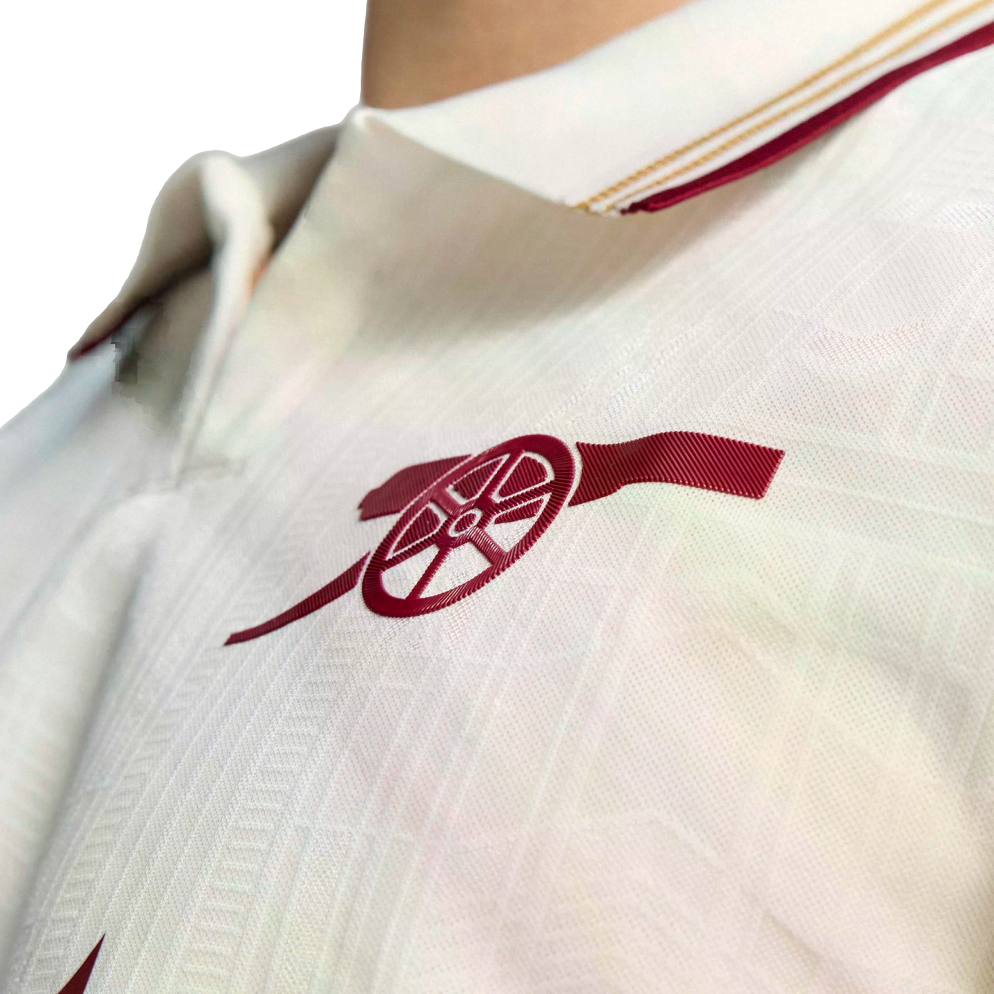 Close-up of a white textured jersey featuring a red Arsenal FC cannon logo on the chest and a collar with thin red and gold trim.