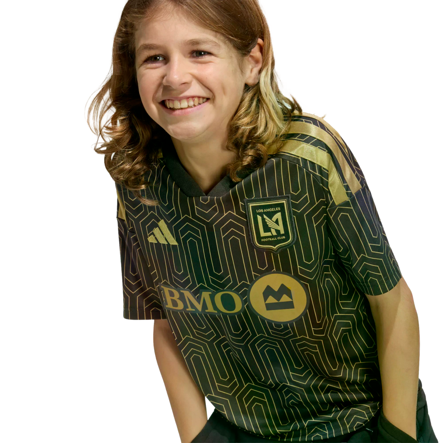 Smiling young person with long wavy hair wearing a black and gold Los Angeles Football Club jersey, leaning forward against a solid black background.