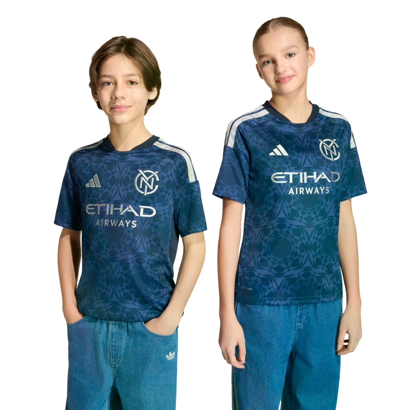 Two children wear matching navy patterned New York City FC soccer jerseys with silver Etihad Airways logos and blue jeans, standing against a black background.