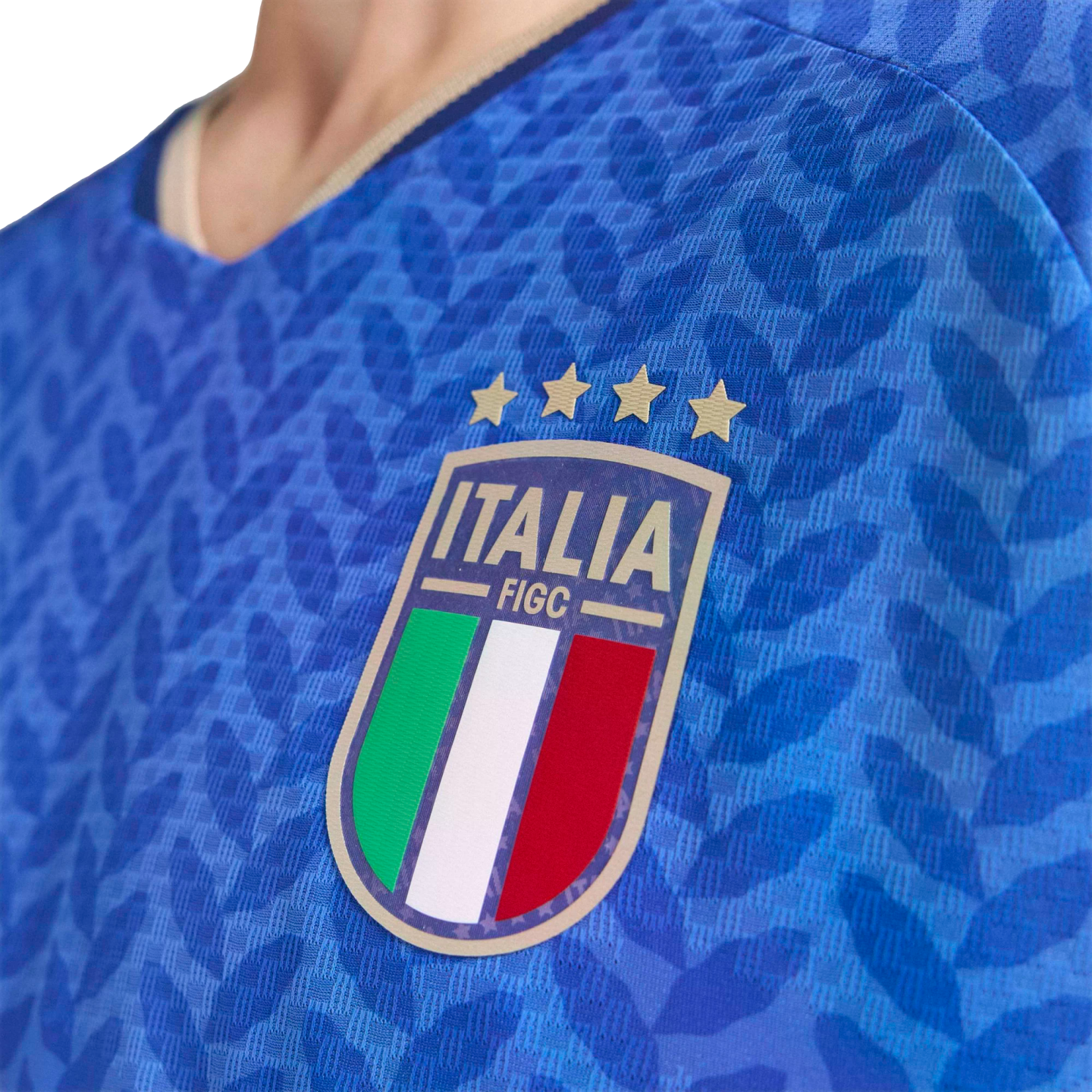 Close-up of a blue Italy national soccer jersey featuring the FIGC crest with four gold stars and a textured leaf pattern.