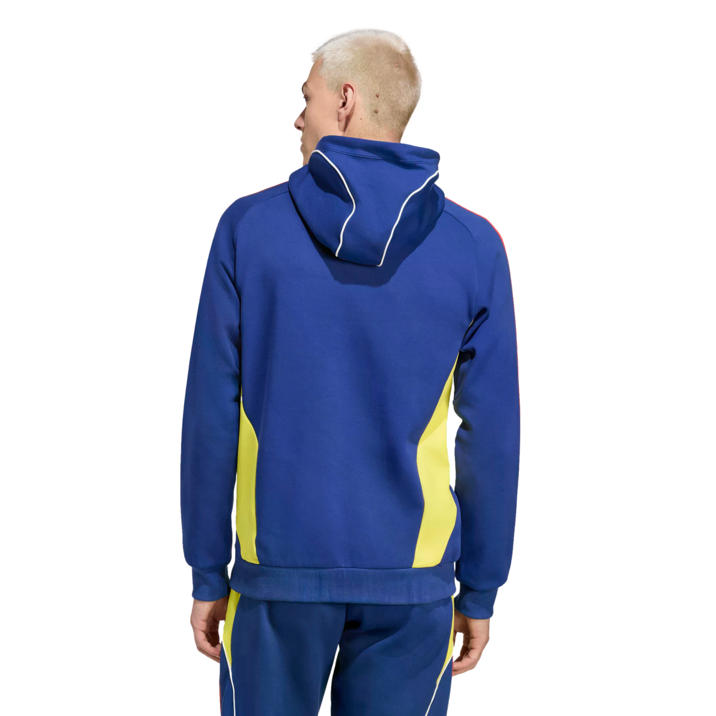 Rear view of a man with blond hair wearing a blue hoodie and matching pants with yellow side panels and white piping, set against a black background.