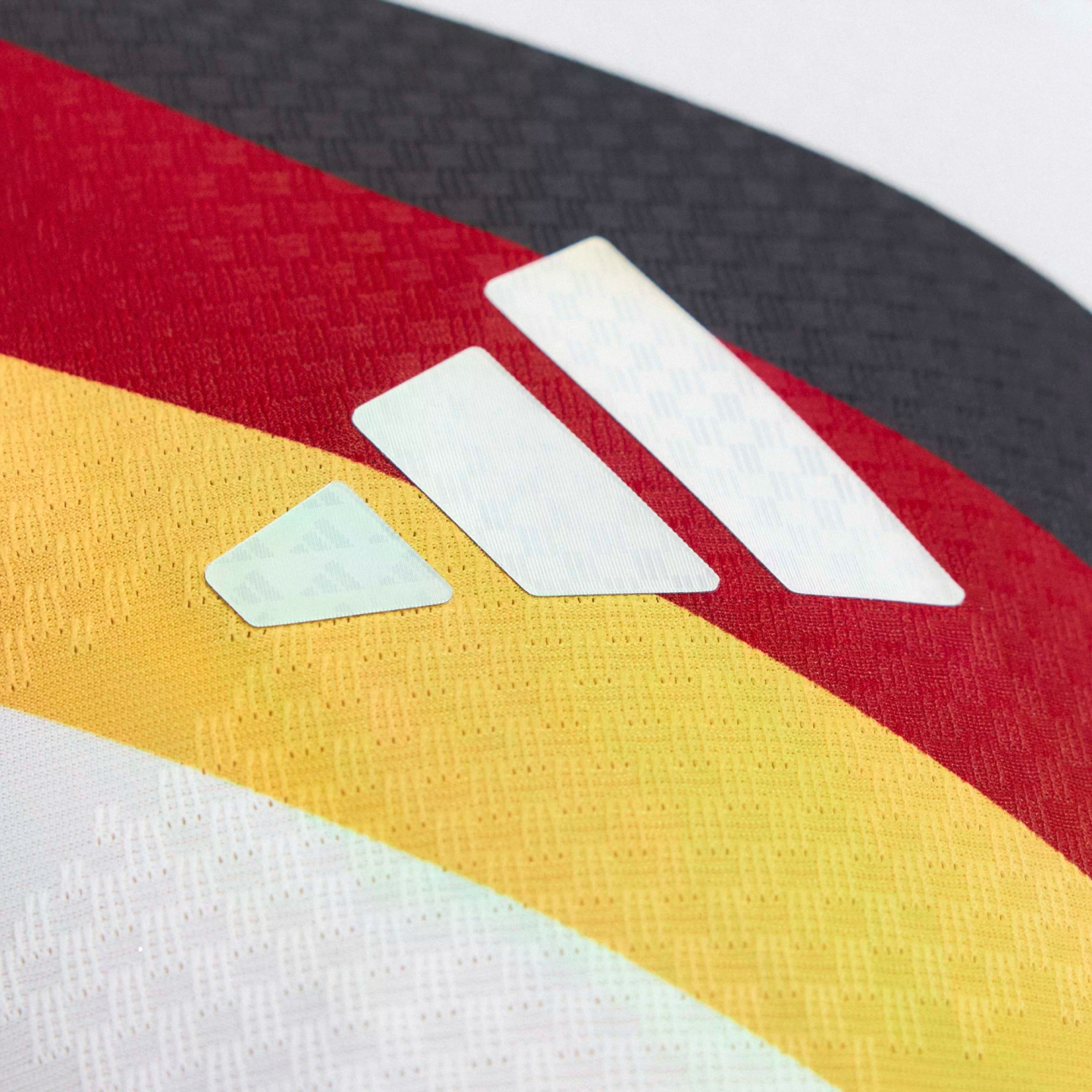White Adidas logo on textured fabric featuring diagonal black, red, and yellow stripes of the German flag.